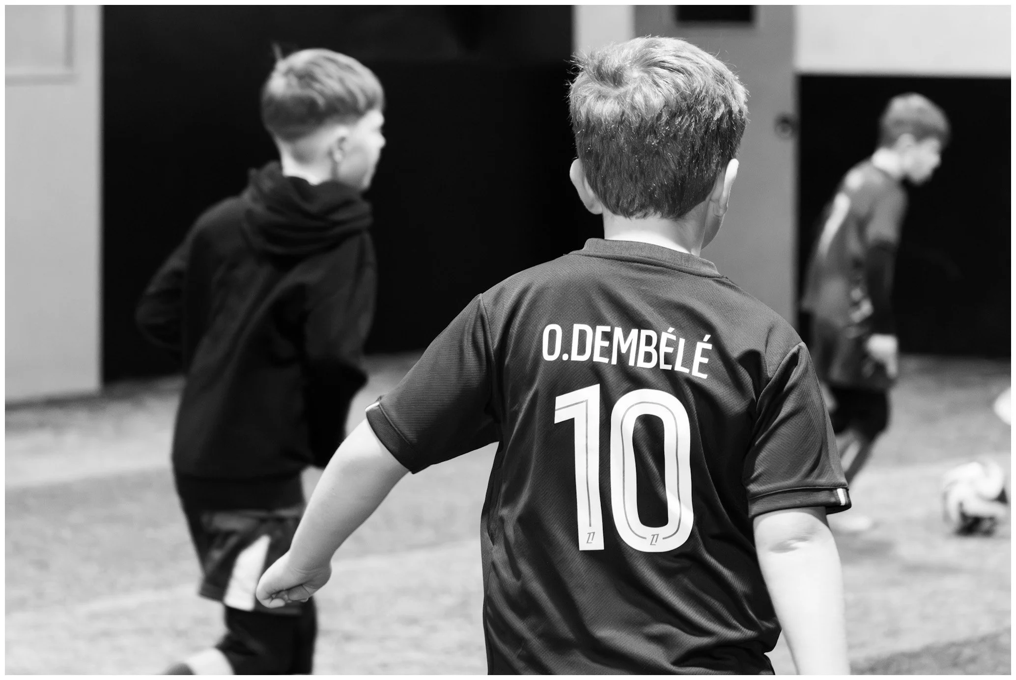 Young boys playing soccer indoors, one boy with a jersey labeled 'O. Dembélé' and the number 10.