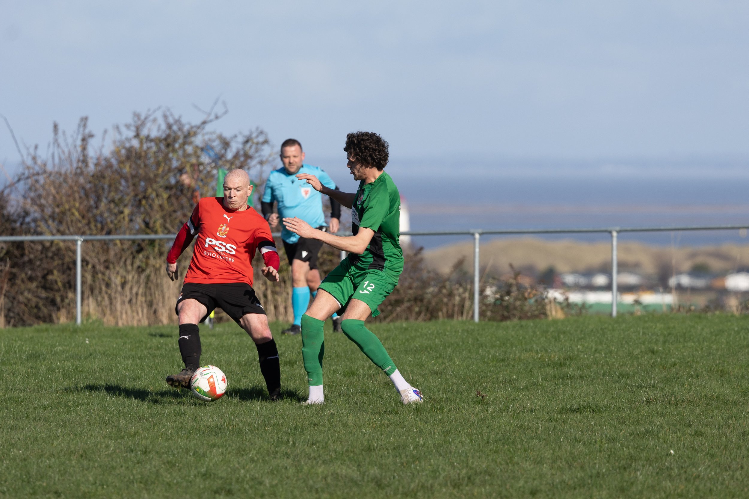 Two soccer players competing for the ball, with a referee observing in the background on the field.