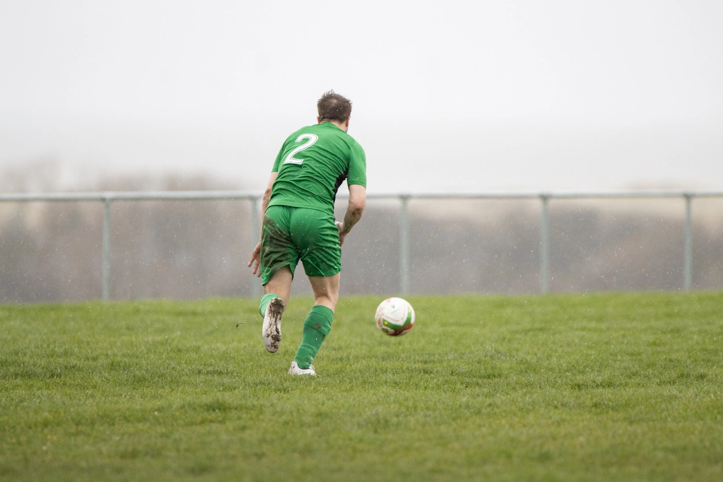 A soccer player in green uniform with the number 2 on his back prepares to kick a soccer ball on a grassy field