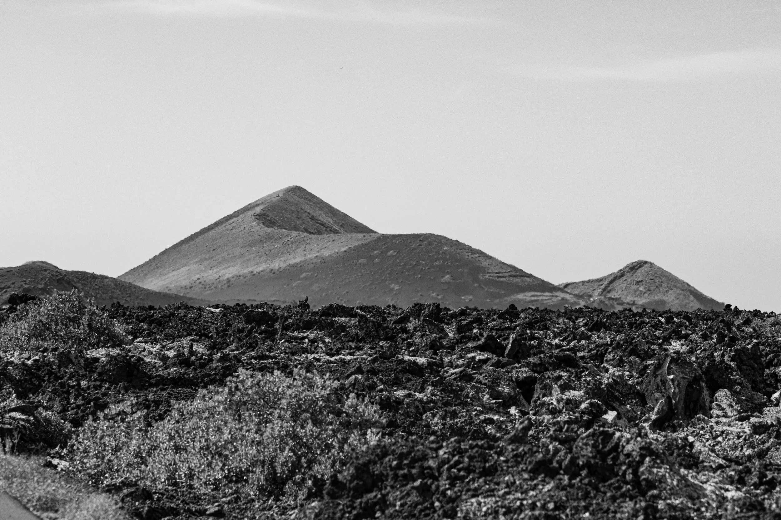 Black and white photograph of volcanic landscape with three mountains in the background and rough lava rocks in the foreground.
