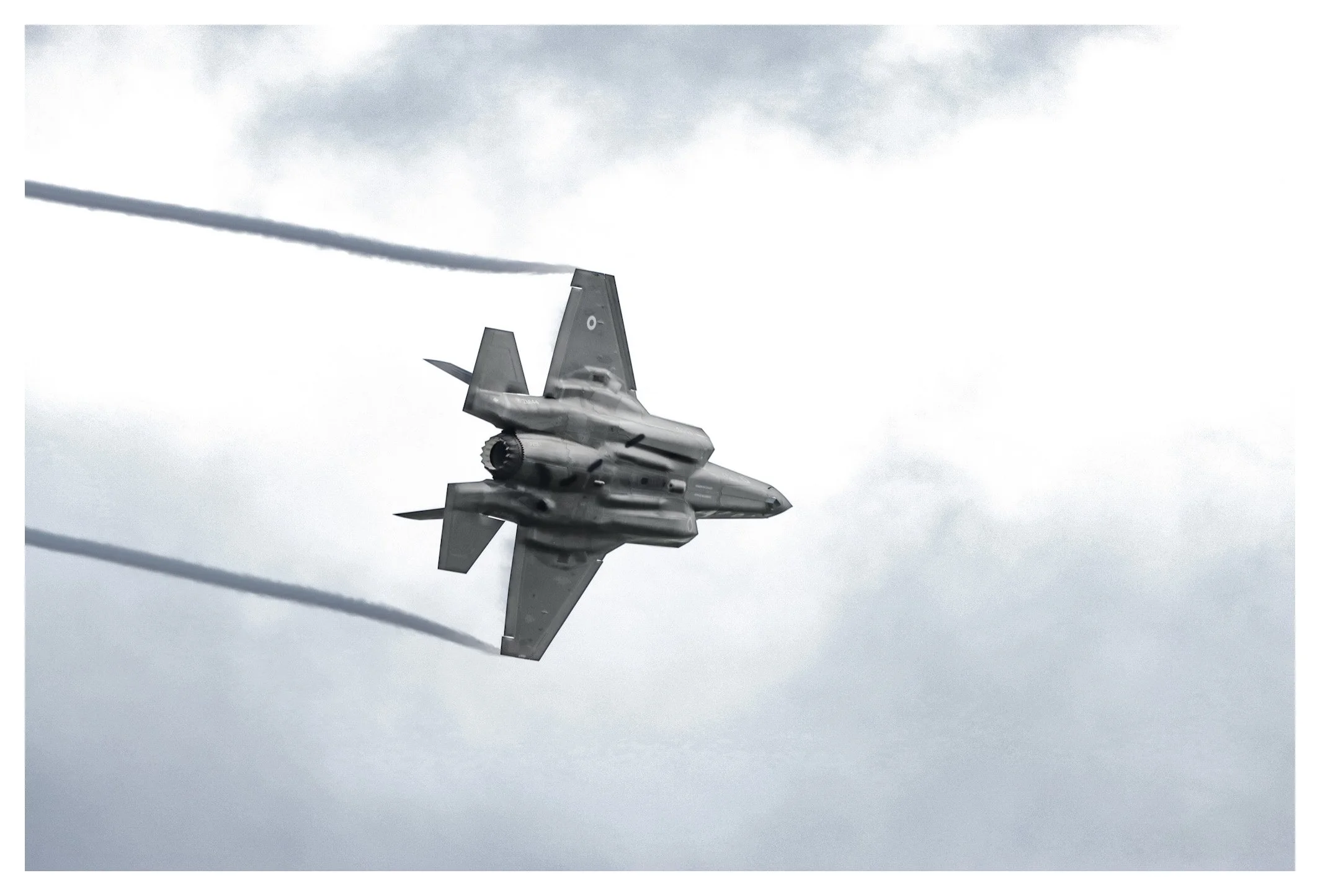 A fighter jet flying at an angle in the sky, leaving dark smoke trails behind it on cloudy weather.