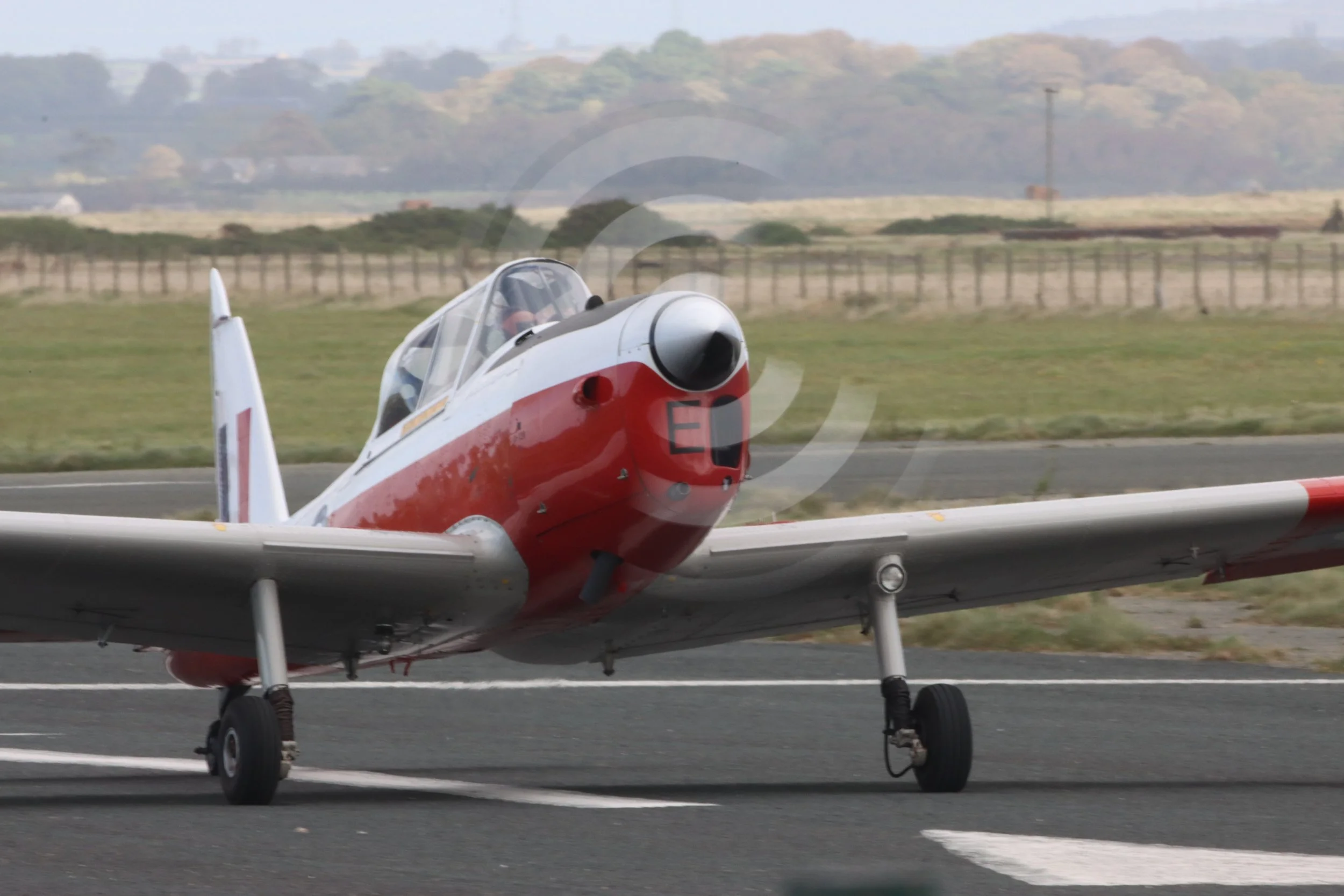 A vintage propeller-driven aircraft on a runway with a grassy field and distant hills in the background.