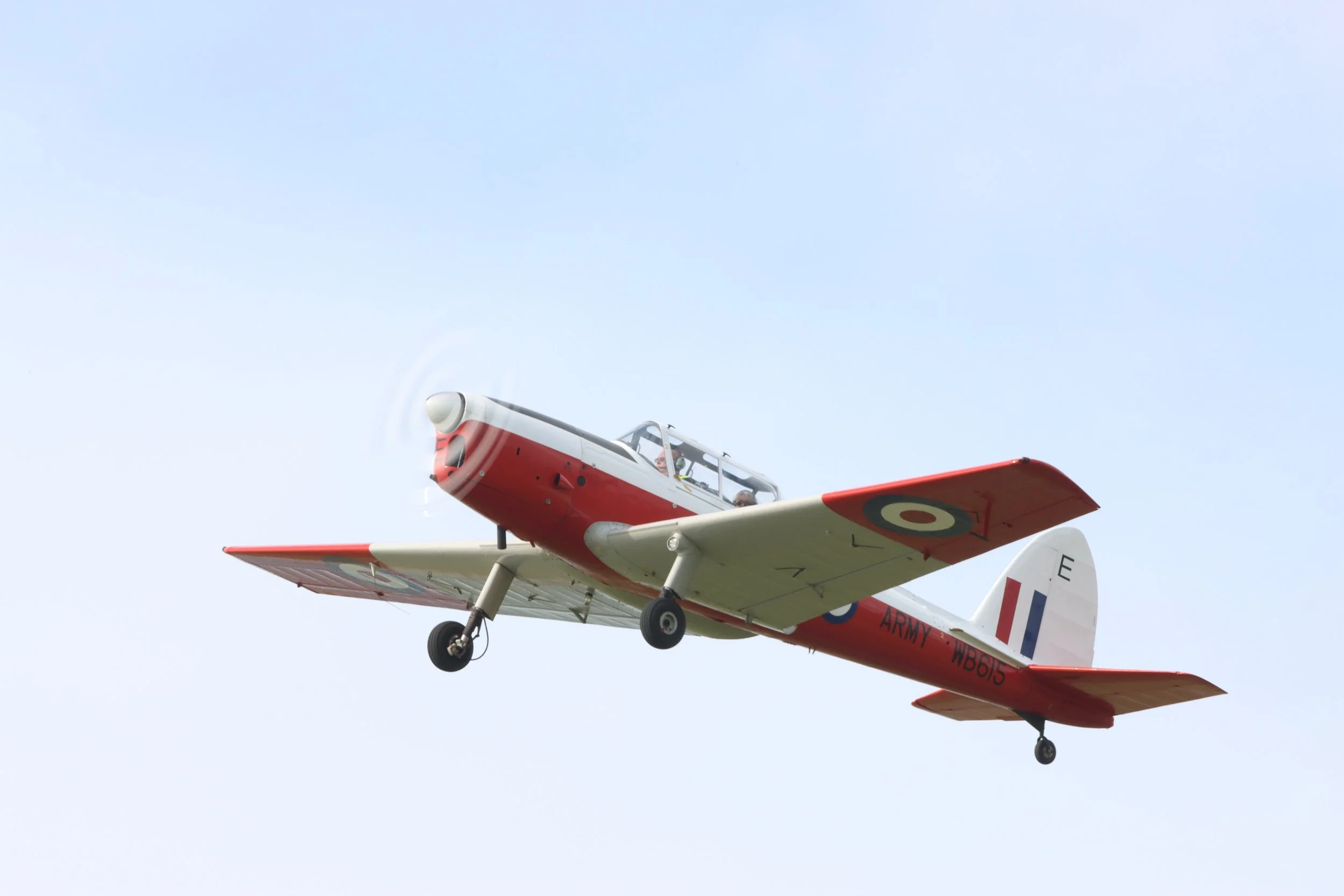 A vintage red and white military training airplane flying in a light blue sky.
