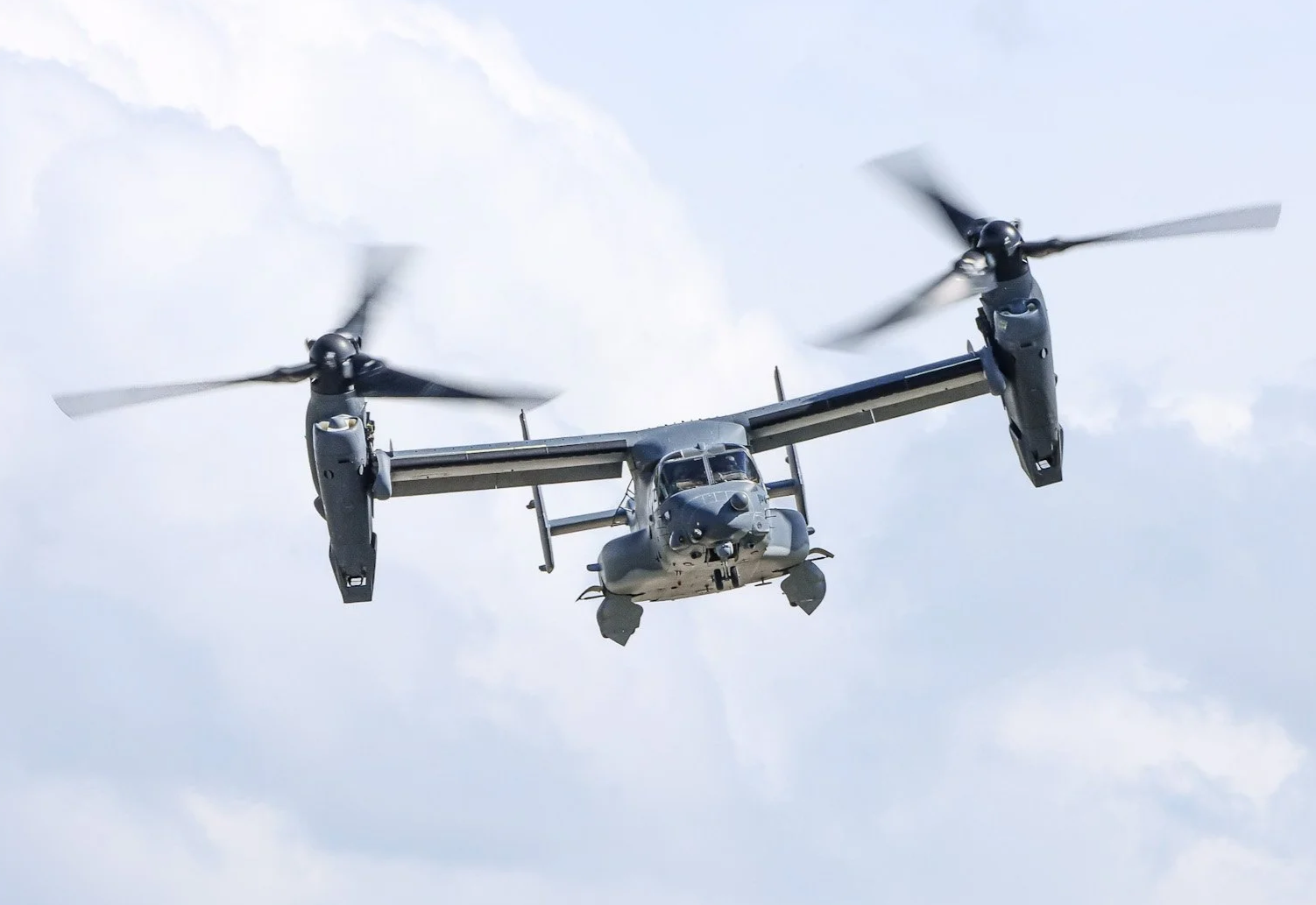 A military tiltrotor aircraft in flight against a cloudy sky.