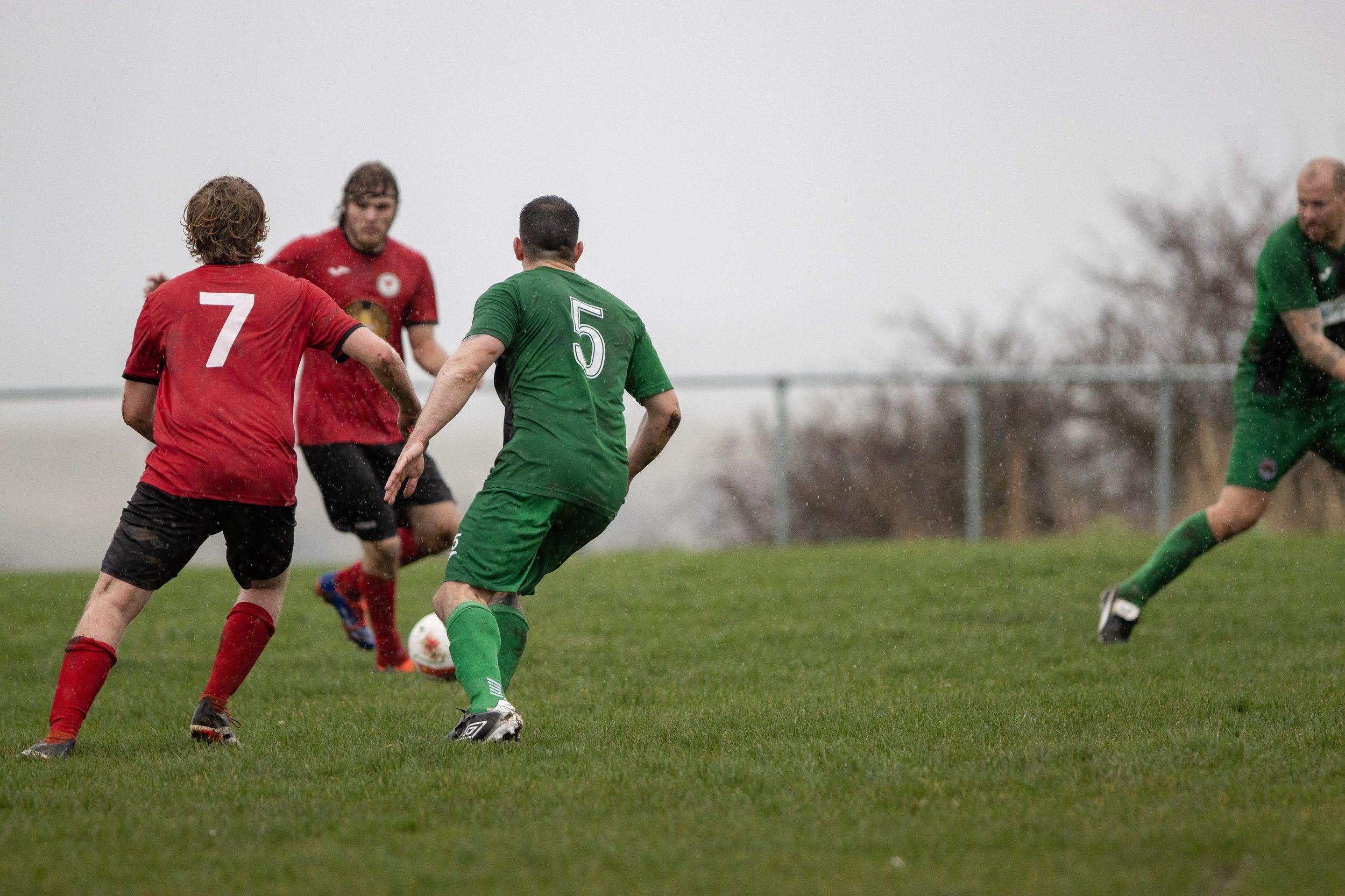 Soccer players in red and green uniforms playing a game on a rainy day.