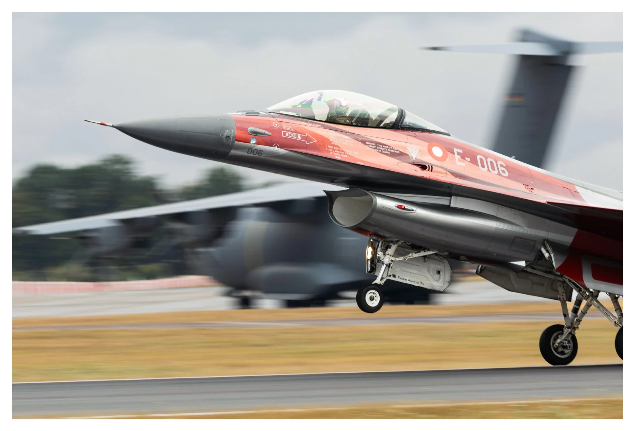 A fighter jet taking off from a runway with a blurred background, showing a crew member inside the cockpit.