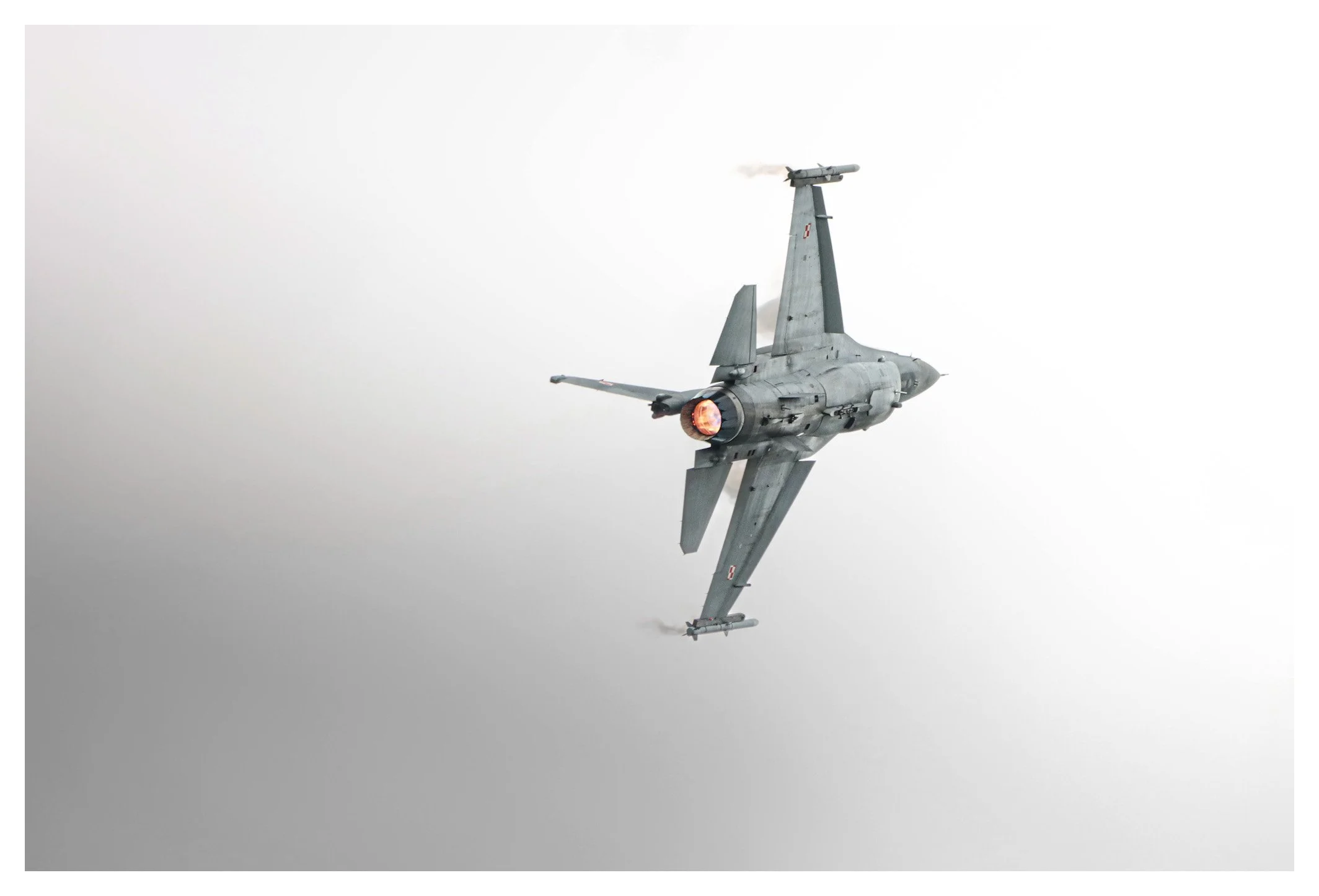 A fighter jet aircraft flying with afterburner engaged, emitting bright flame from its exhaust, against a mostly clear sky.