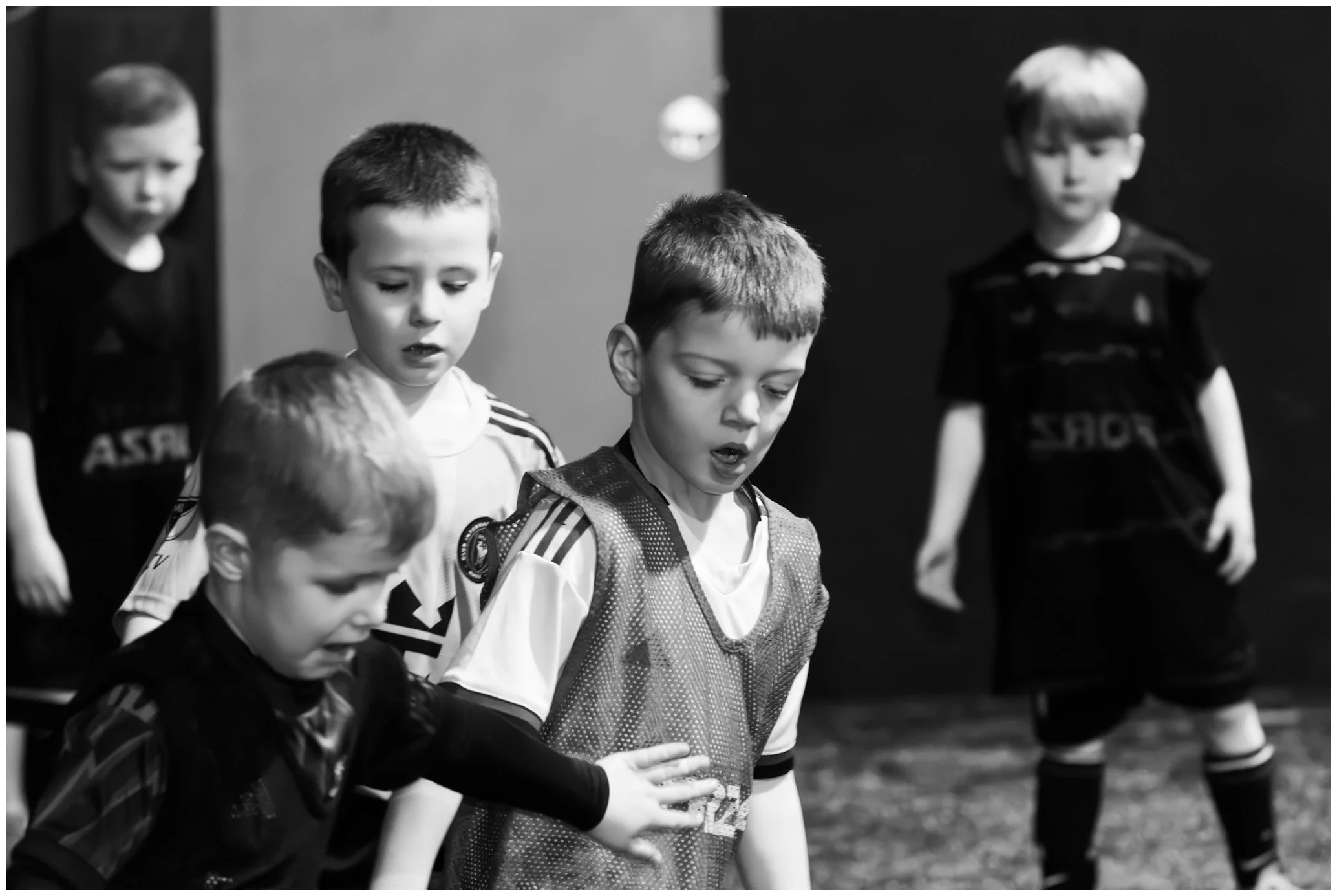 Black and white photo of five young boys wearing sports jerseys, standing on a sports field, looking down with serious expressions.