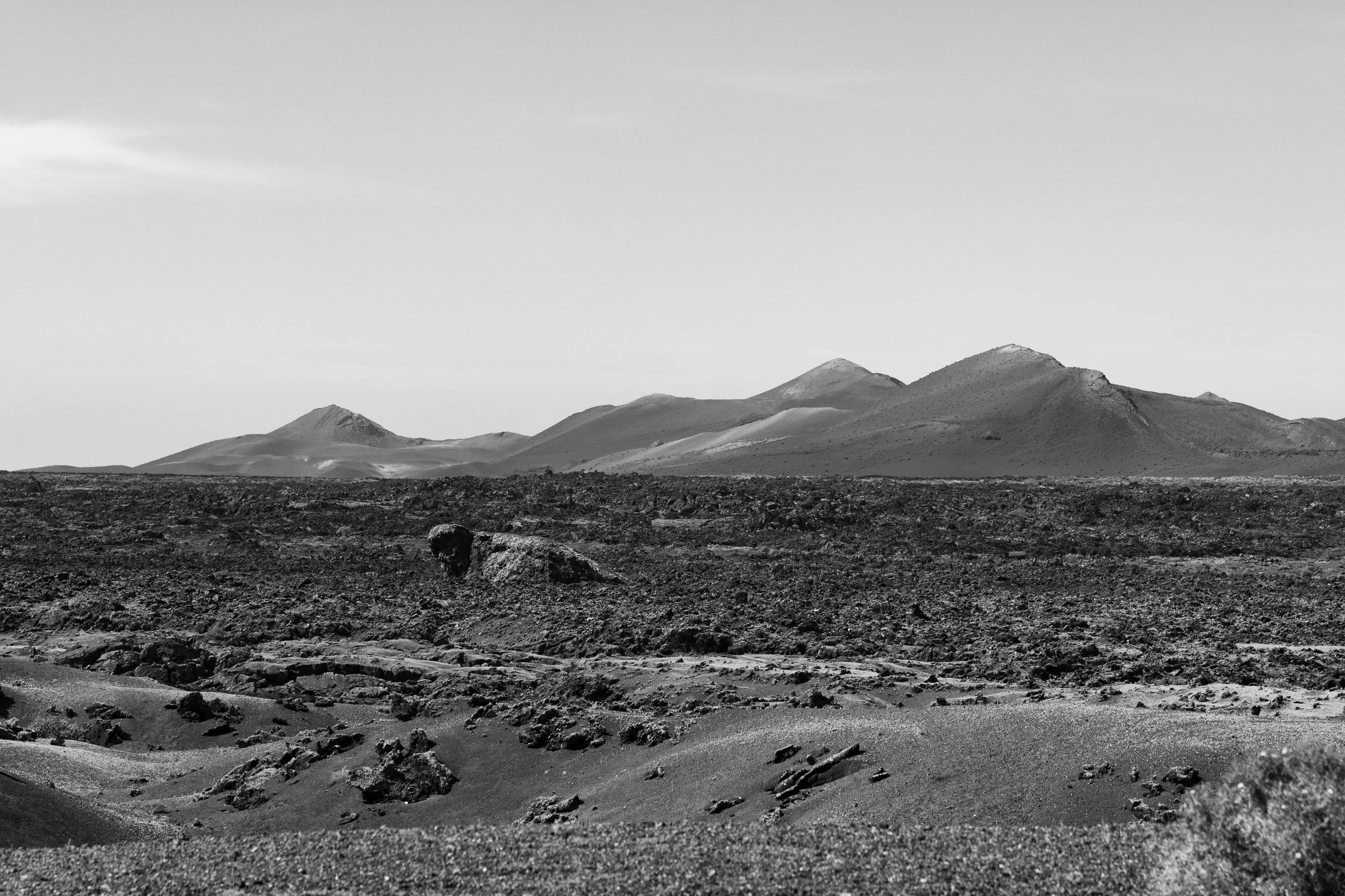 Black and white photo of volcanic landscape with mountains in the distance and rough terrain in the foreground.
