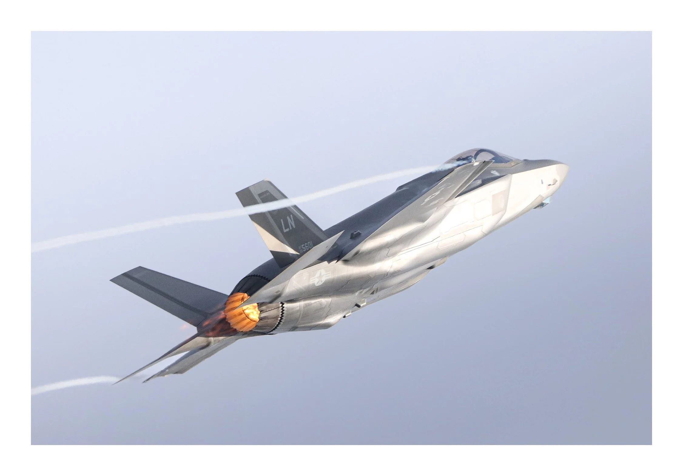 A fighter jet airplane flying in the sky with afterburner flames visible at the engine exhaust, leaving white contrails behind.
