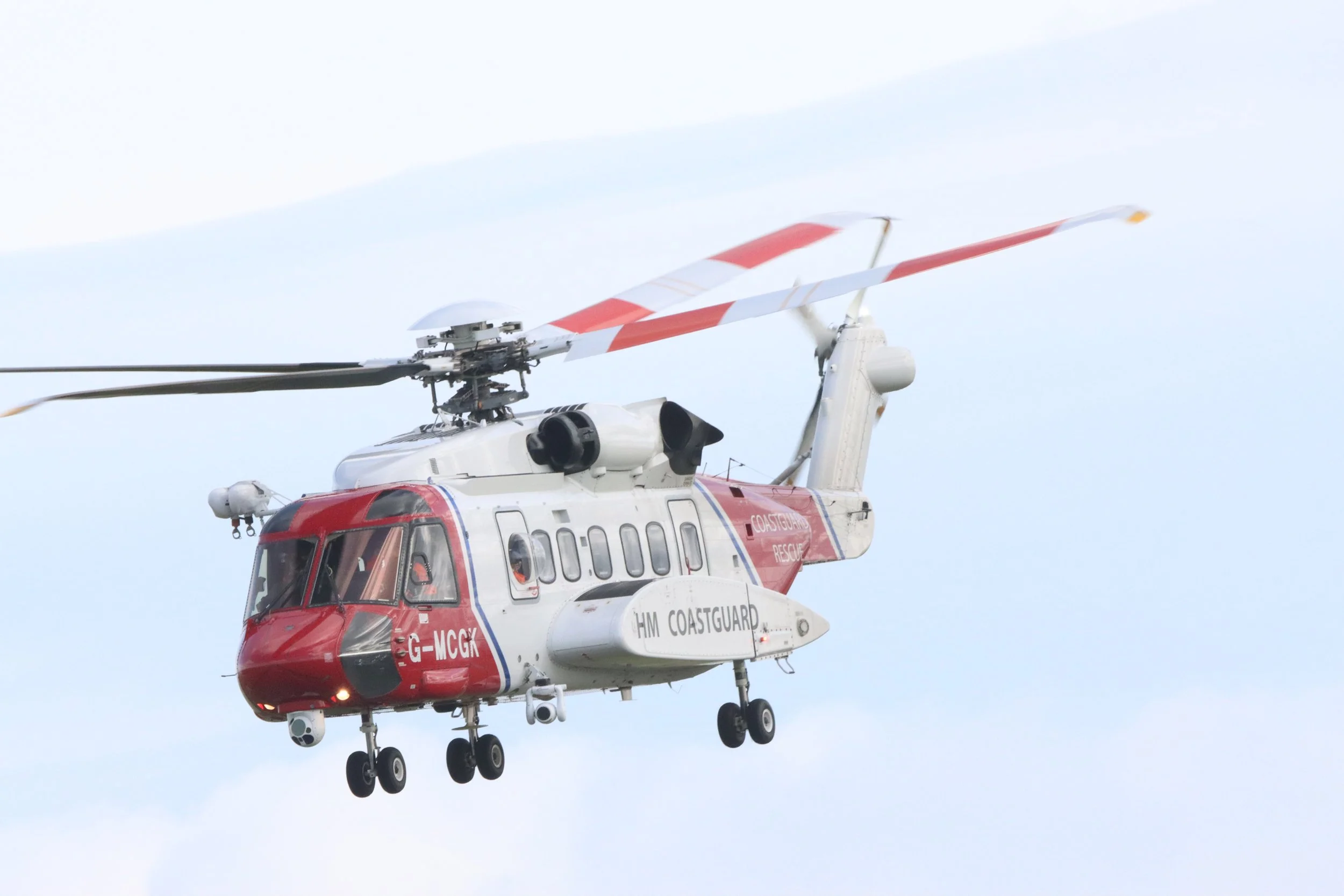 A red and white coastguard rescue helicopter flying in the sky.