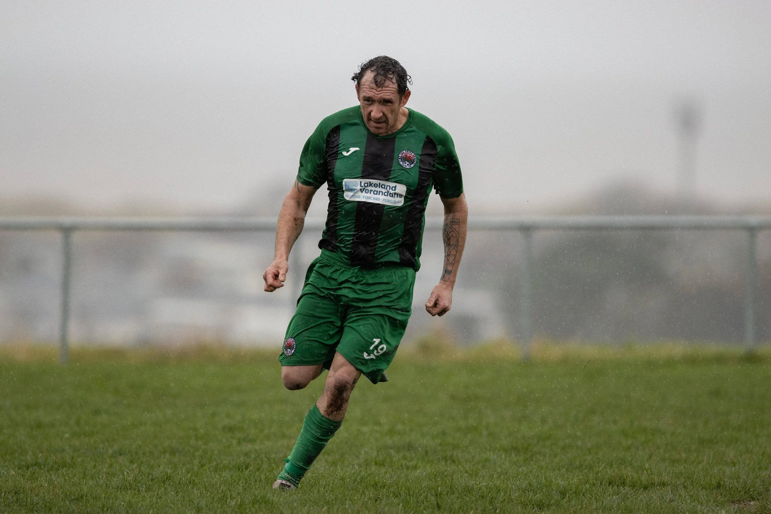 Soccer player in green uniform celebrating on the field in rainy weather.