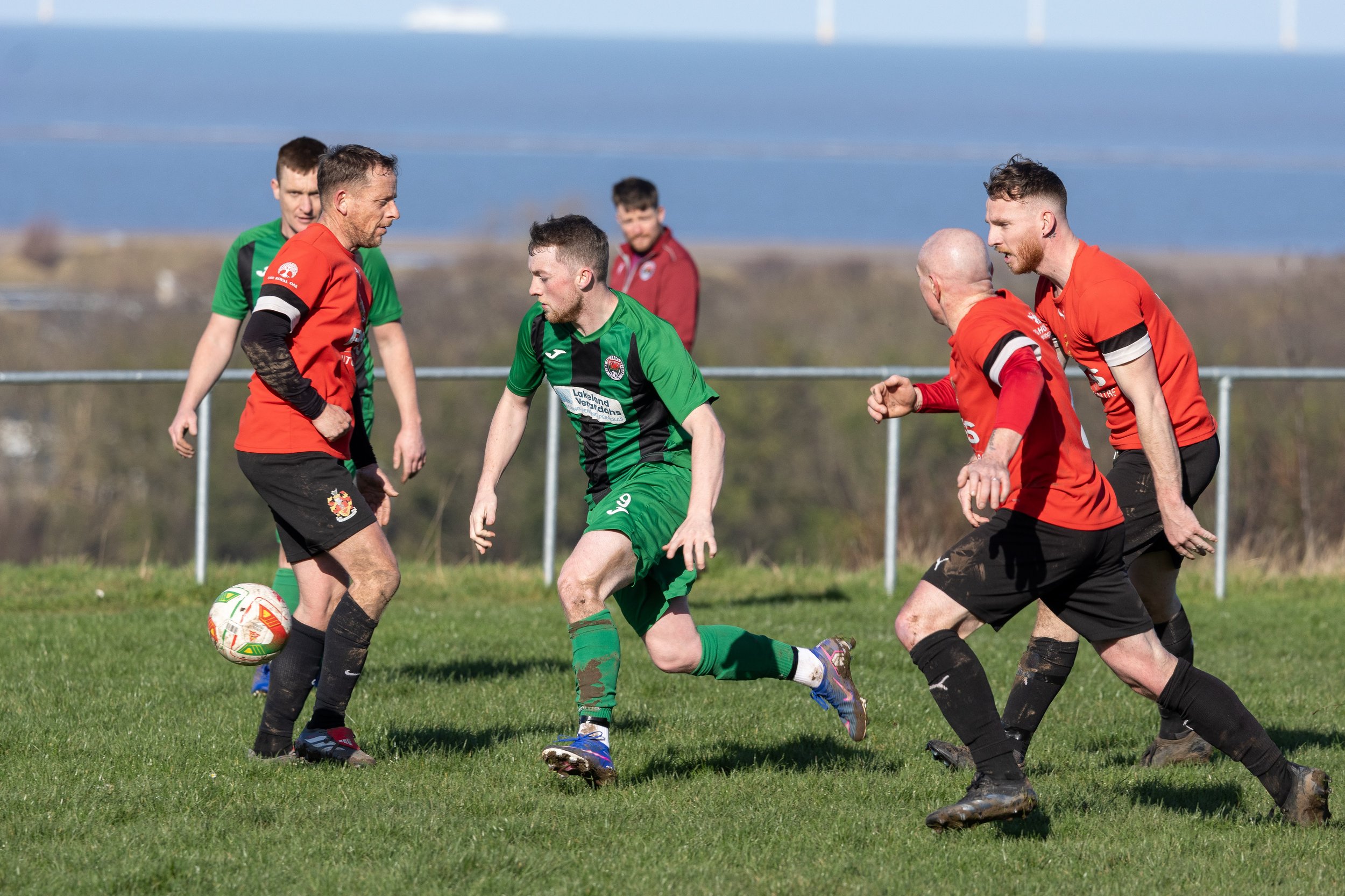 Soccer game with players in green and red jerseys competing for the ball on a grassy field.