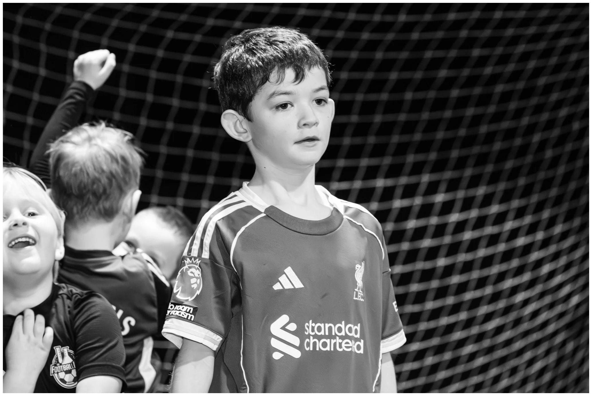 Young boys in football jerseys, one with a Liverpool crest, standing in front of a net, with one boy raising his fist.