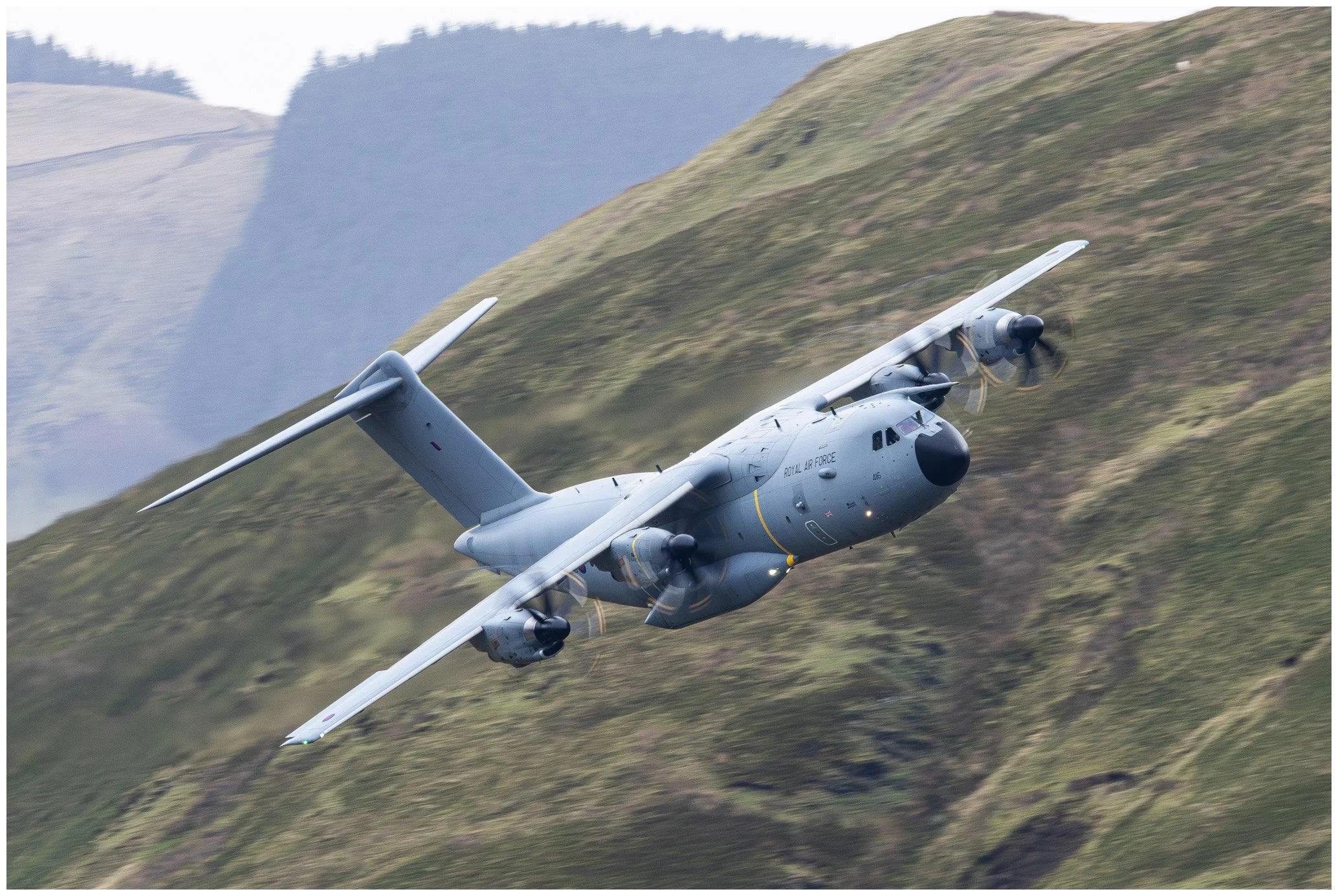 A military cargo airplane flying over green mountains.