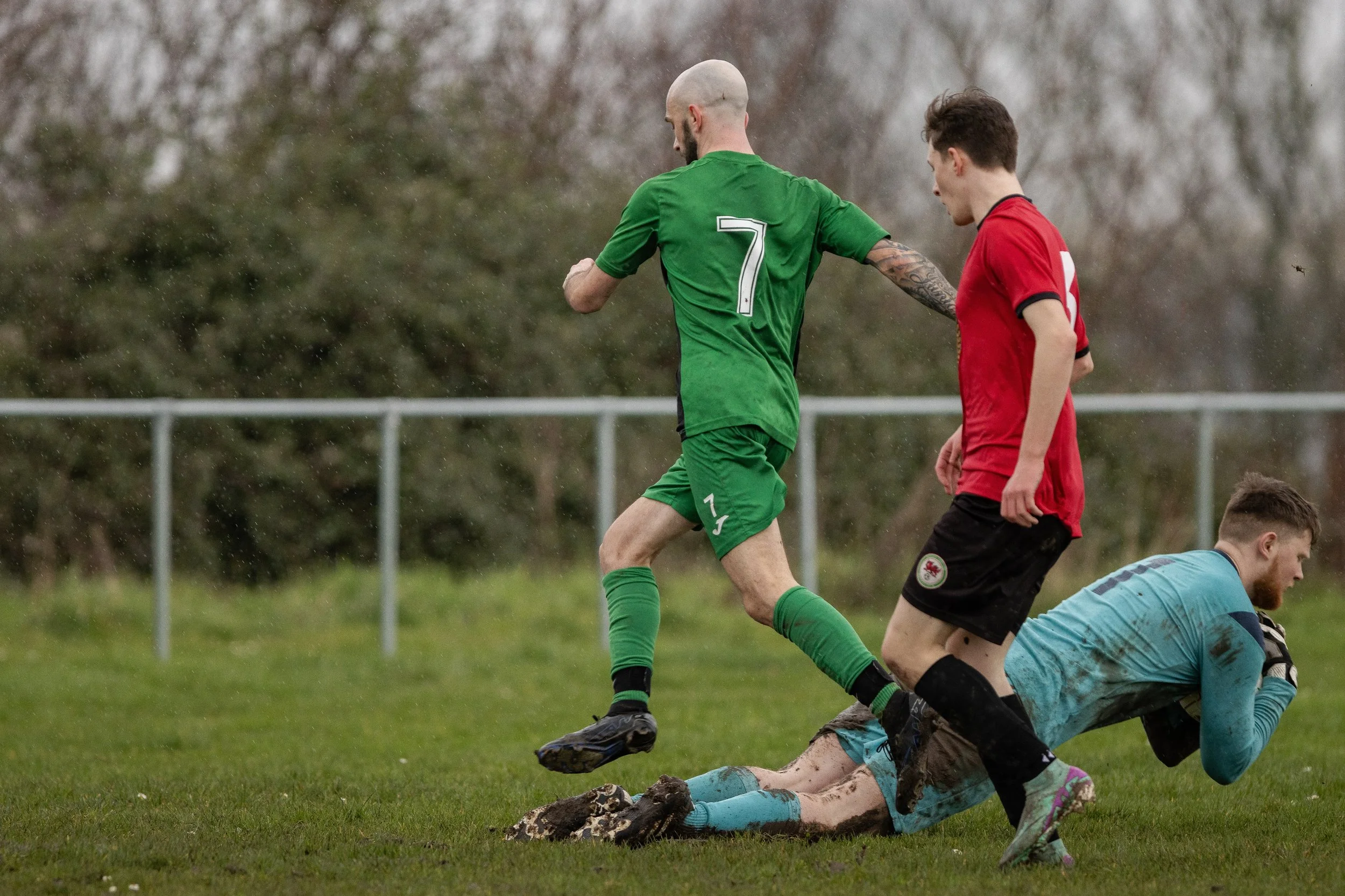 Soccer players battling for the ball on a muddy field during a match.