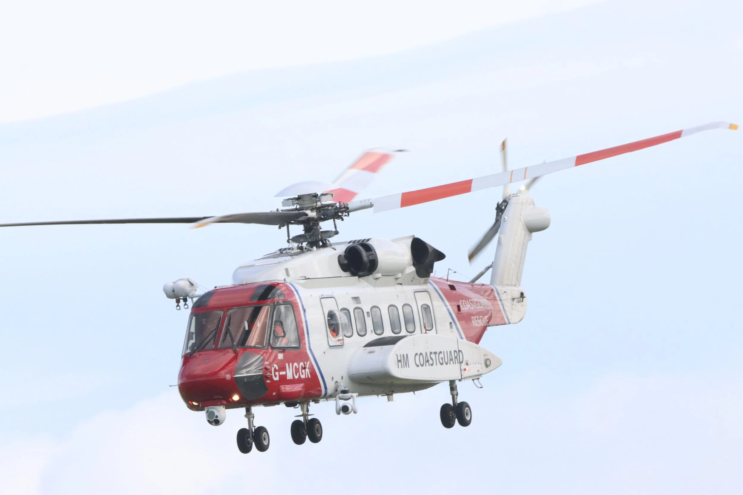 A helicopter painted in red and white with 'HM Coastguard' written on the side, flying in the sky.