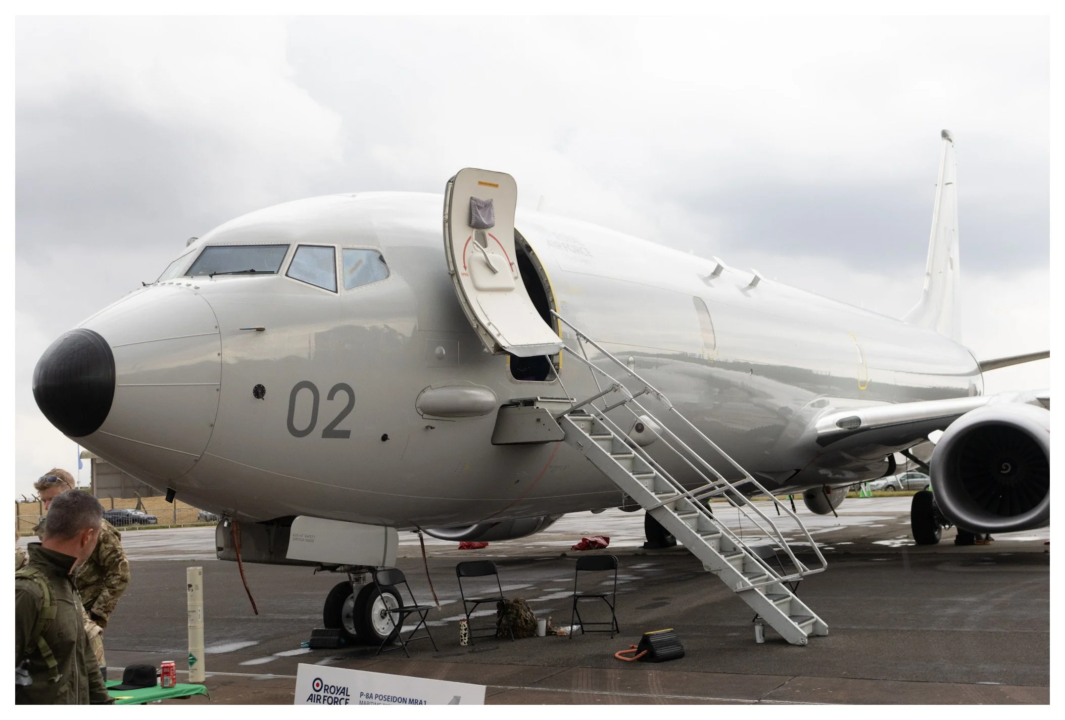 Military aircraft on the tarmac with personnel nearby and stairs leading to the open cargo door.