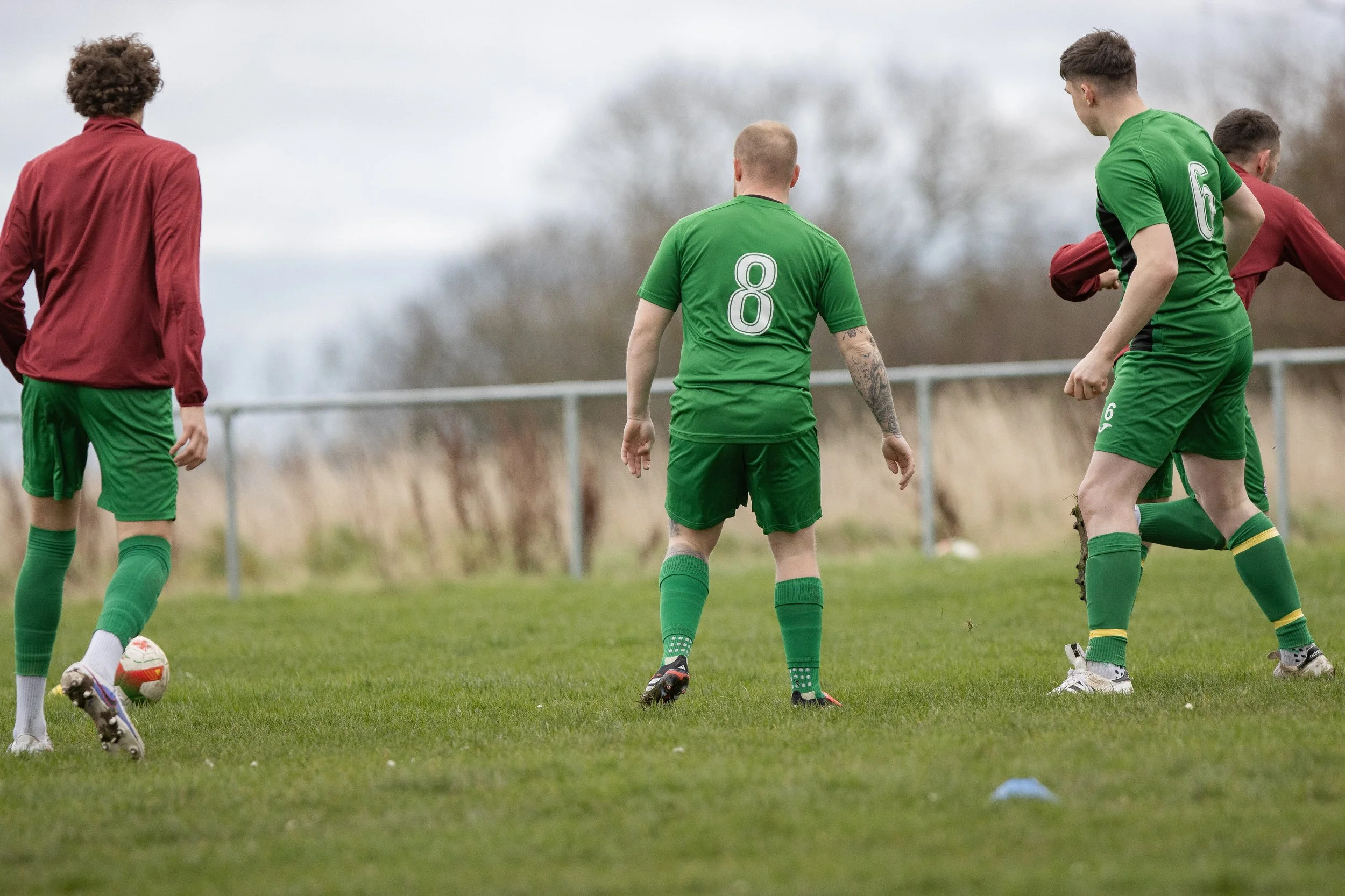 Soccer players in green and red uniforms practicing on a grass field during daytime.