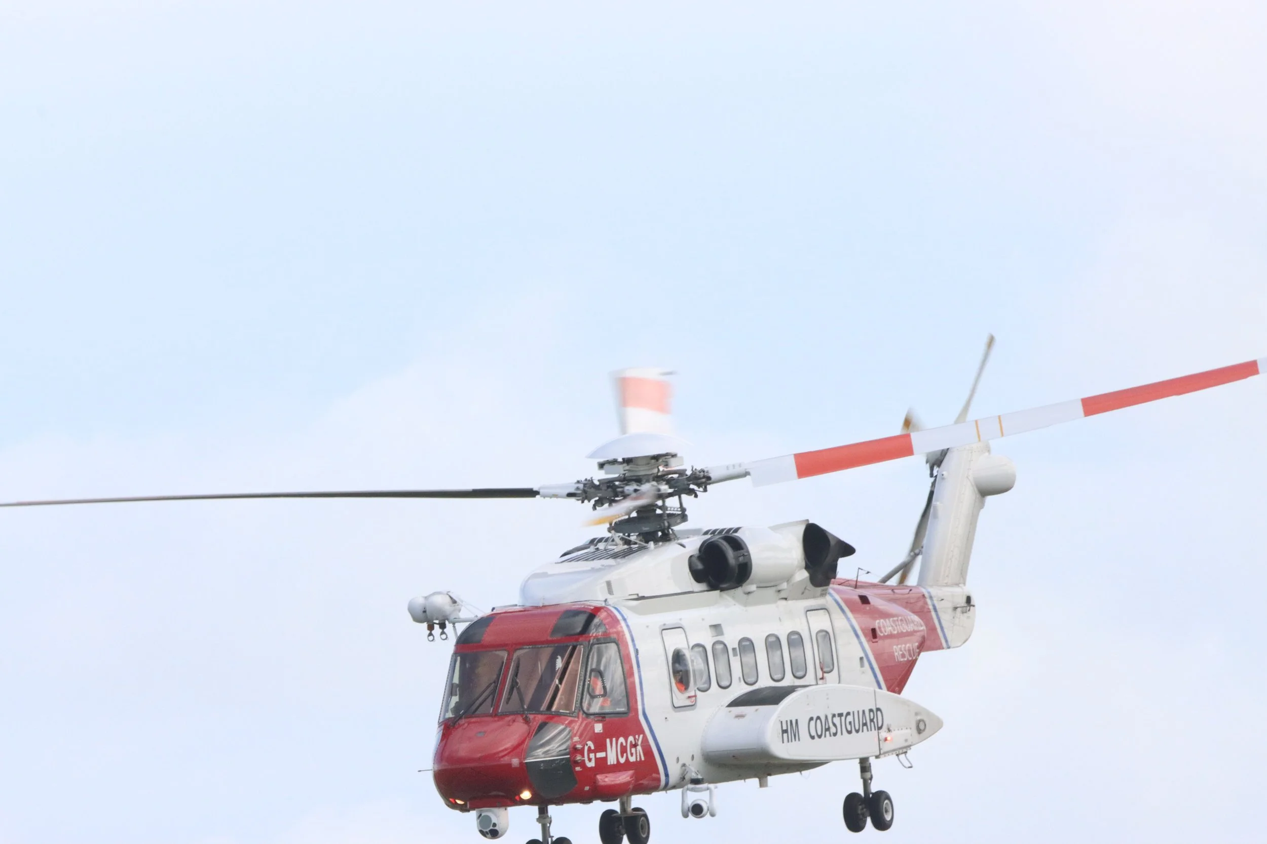 A white helicopter with red accents, marked HM Coastguard, flying against a cloudy sky.