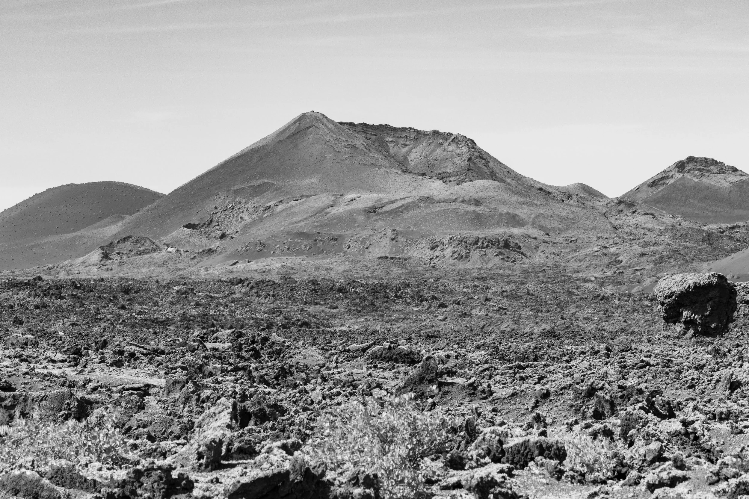 Black and white photo of a desert landscape with rugged, rocky terrain and mountains in the background.