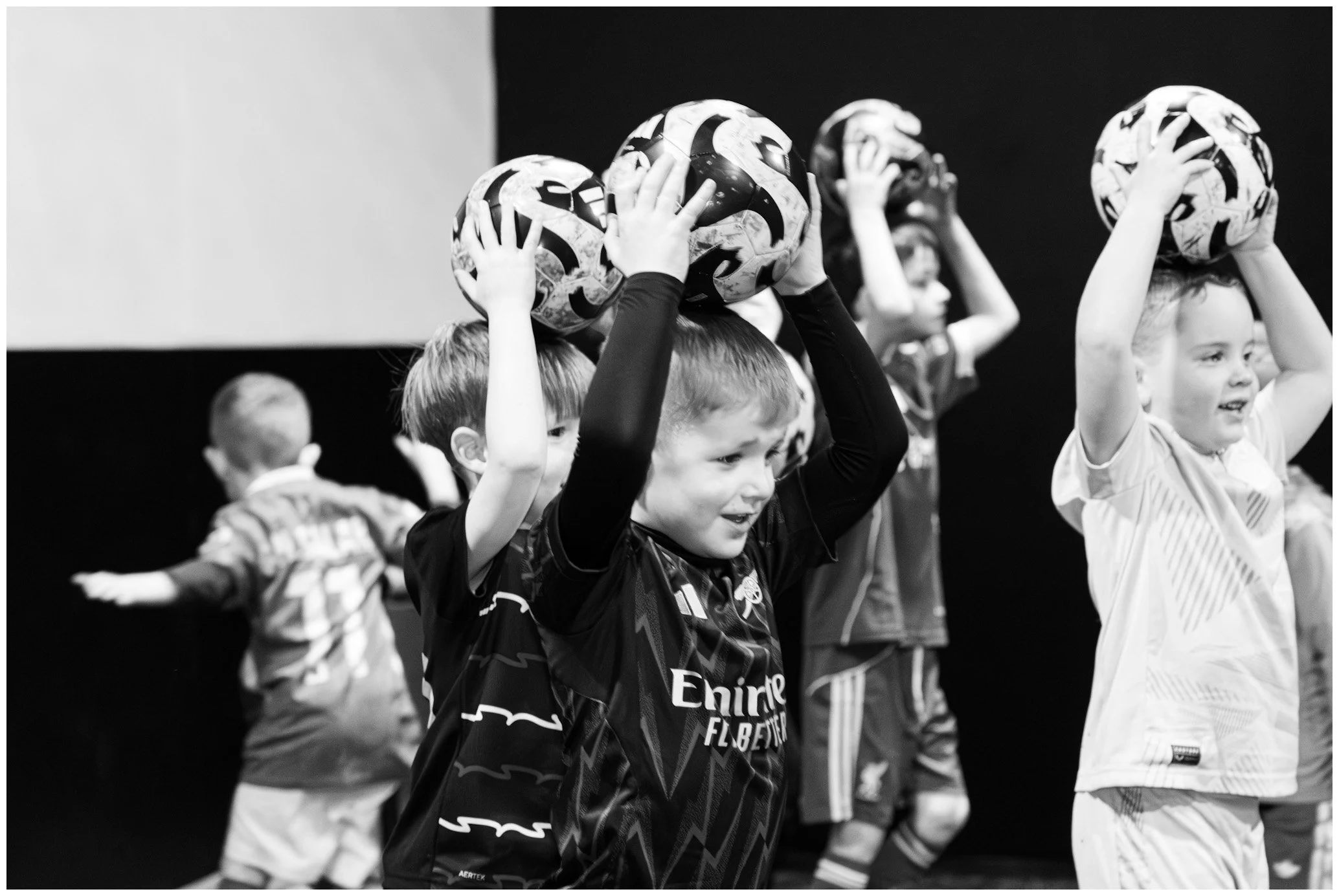 Children participating in a soccer training session, holding soccer balls above their heads