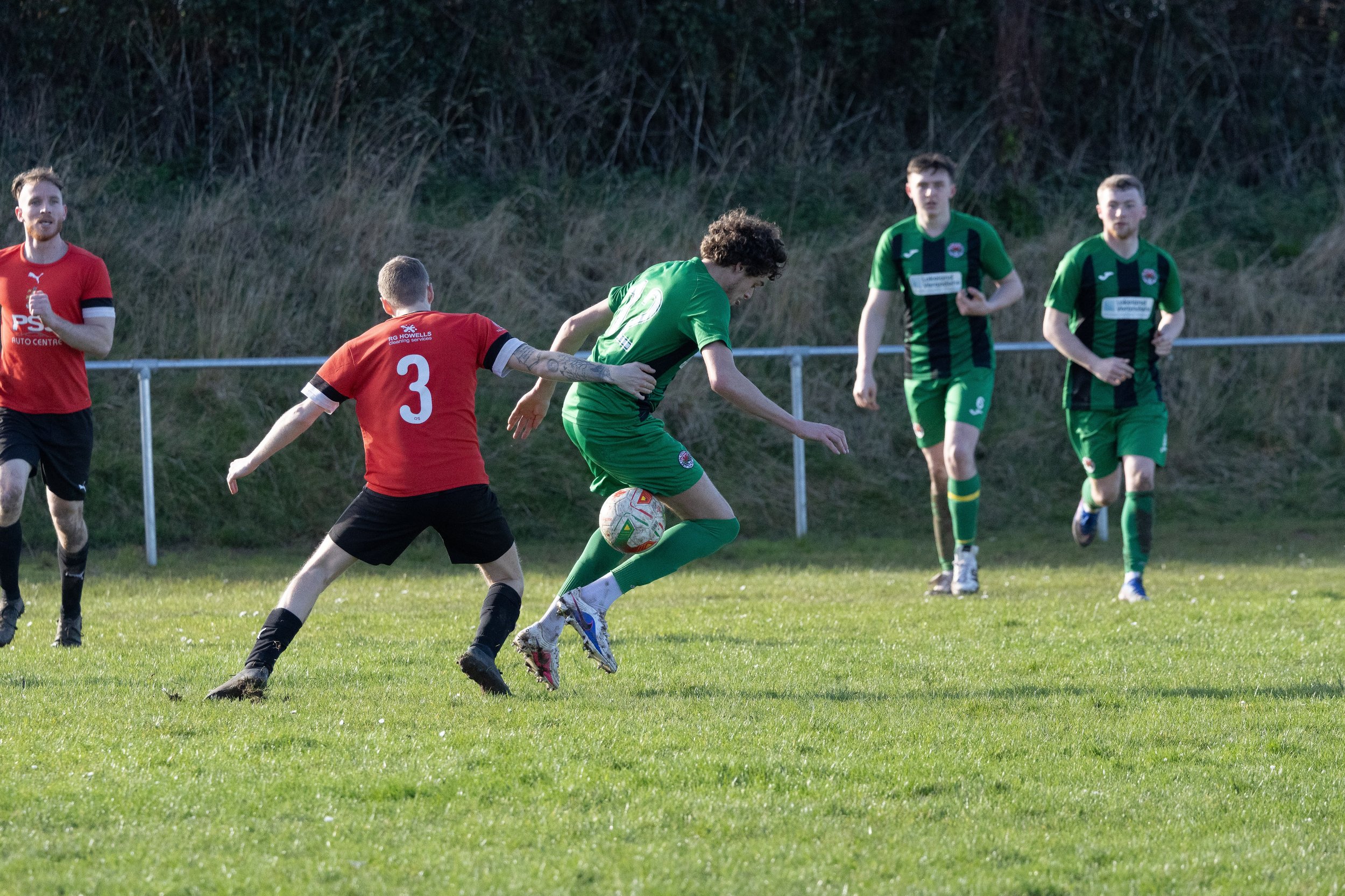 Soccer match with players in green and red uniforms competing for the ball on a grassy field.