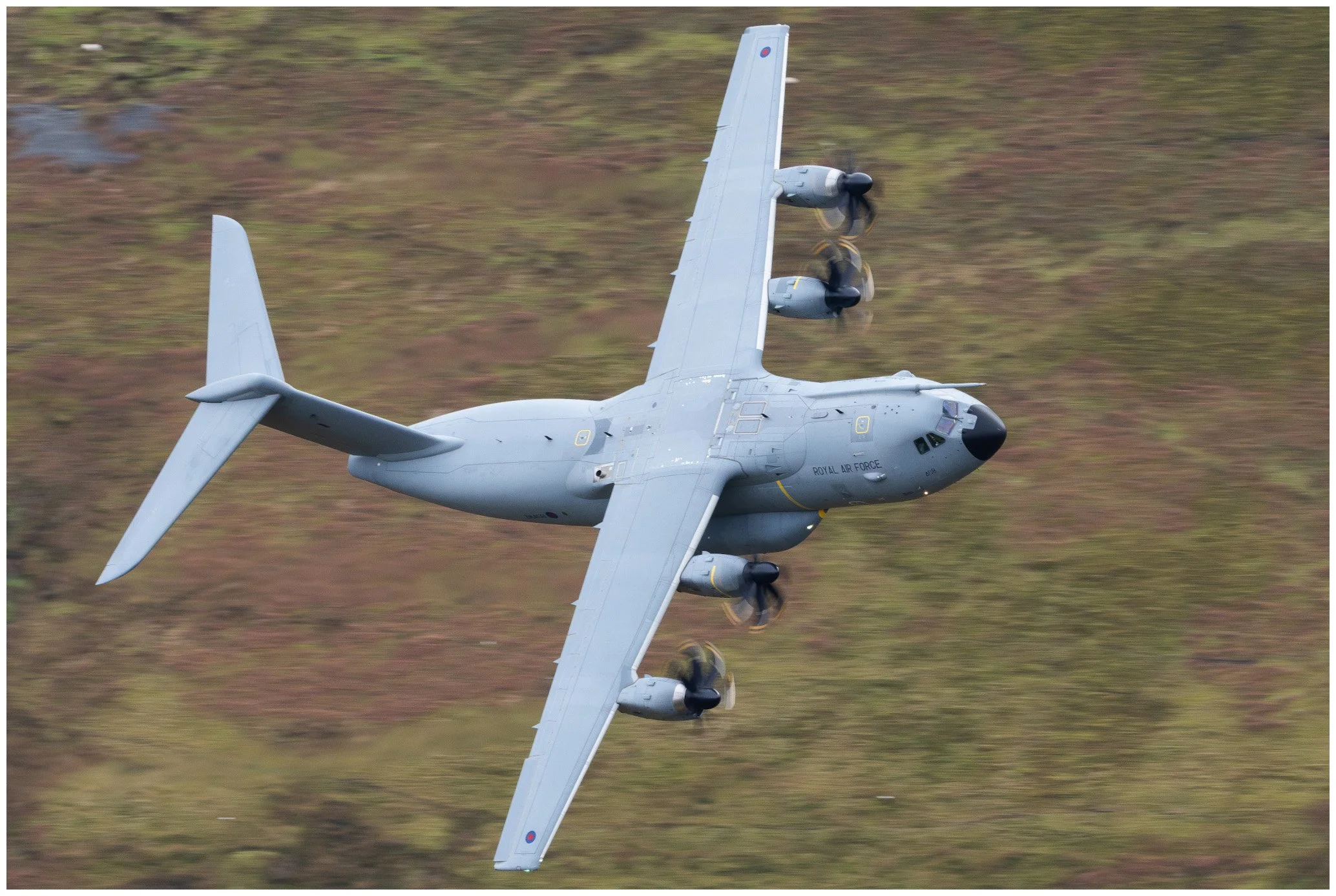 A gray military aircraft flying over a grassy landscape.