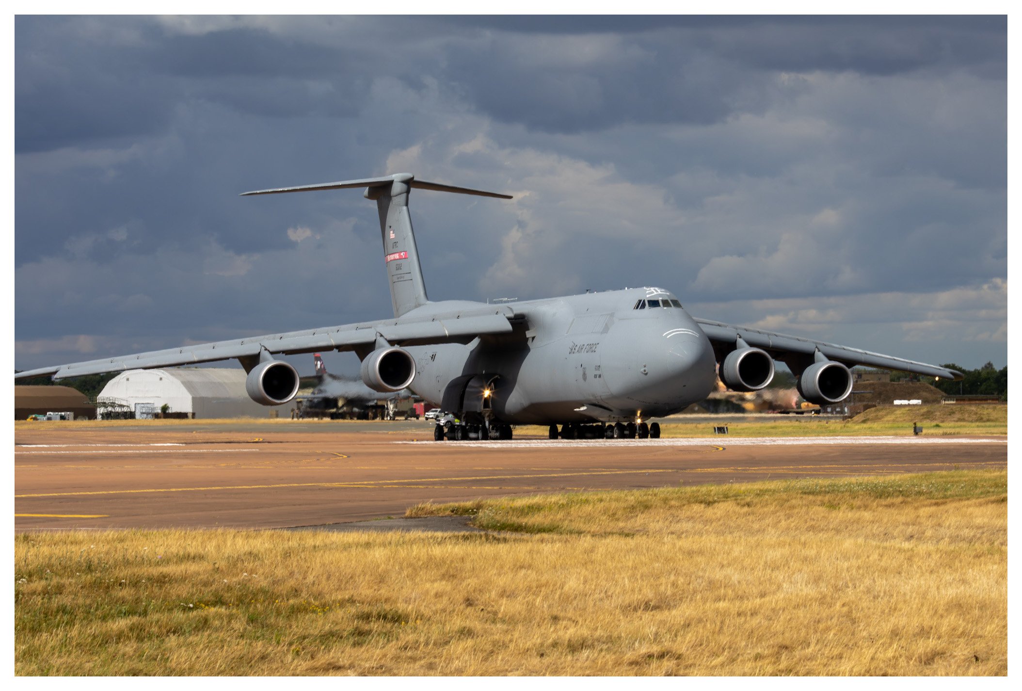 A large military cargo aircraft on a runway during daytime with a cloudy sky.