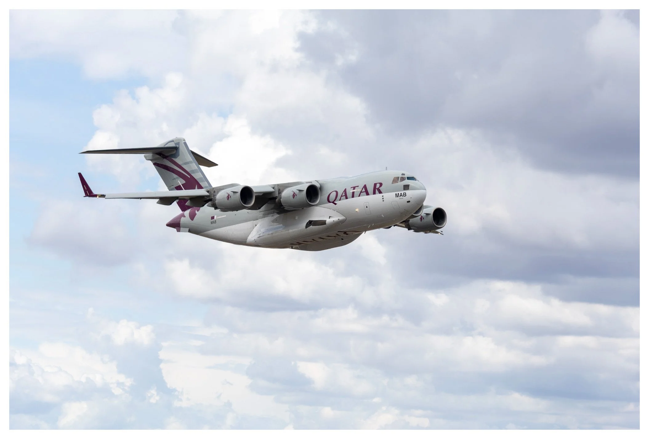 Qatar Airlines cargo airplane flying in a cloudy sky.