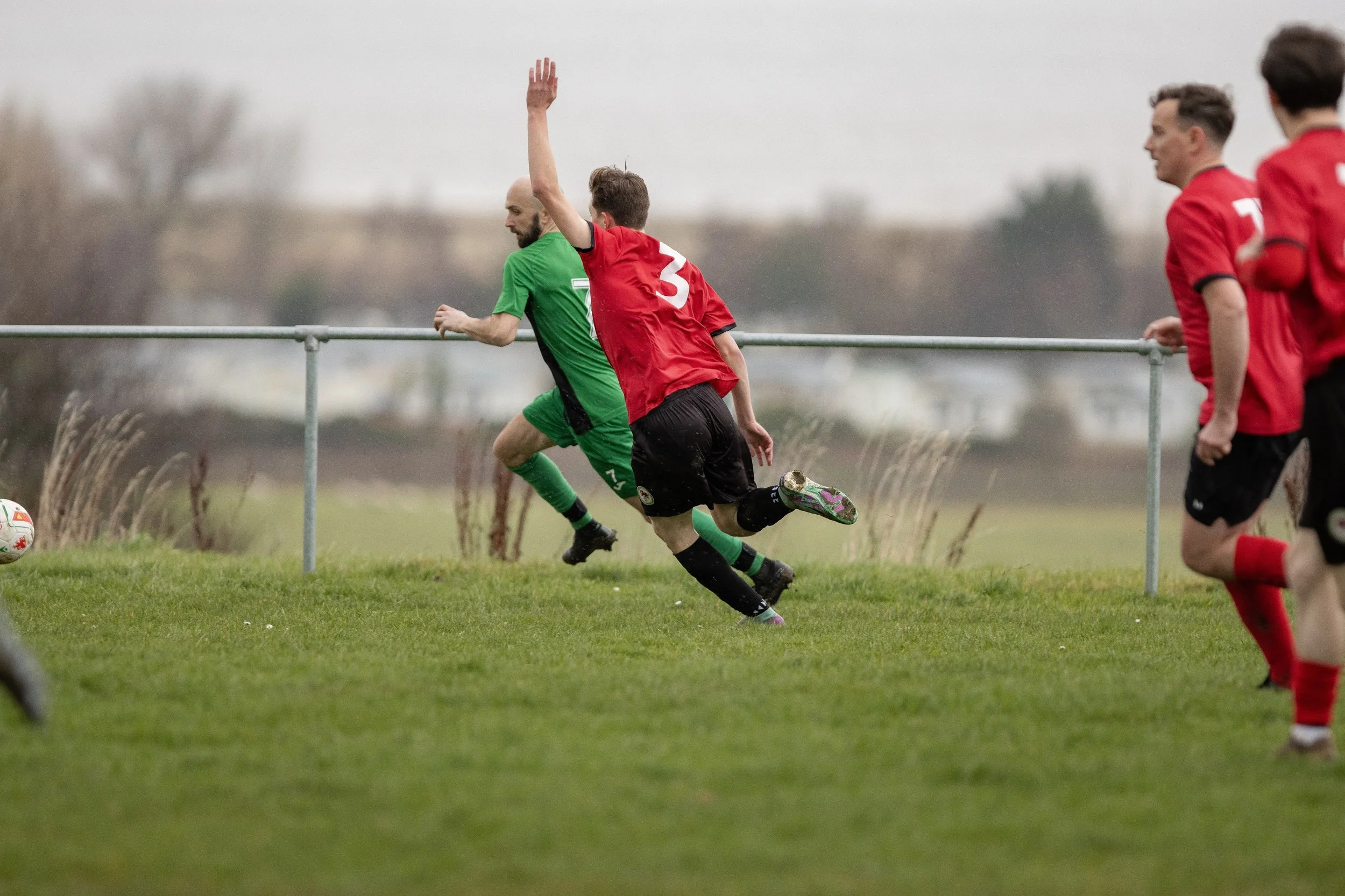 Soccer players in green and red uniforms competing near the sideline of the field.