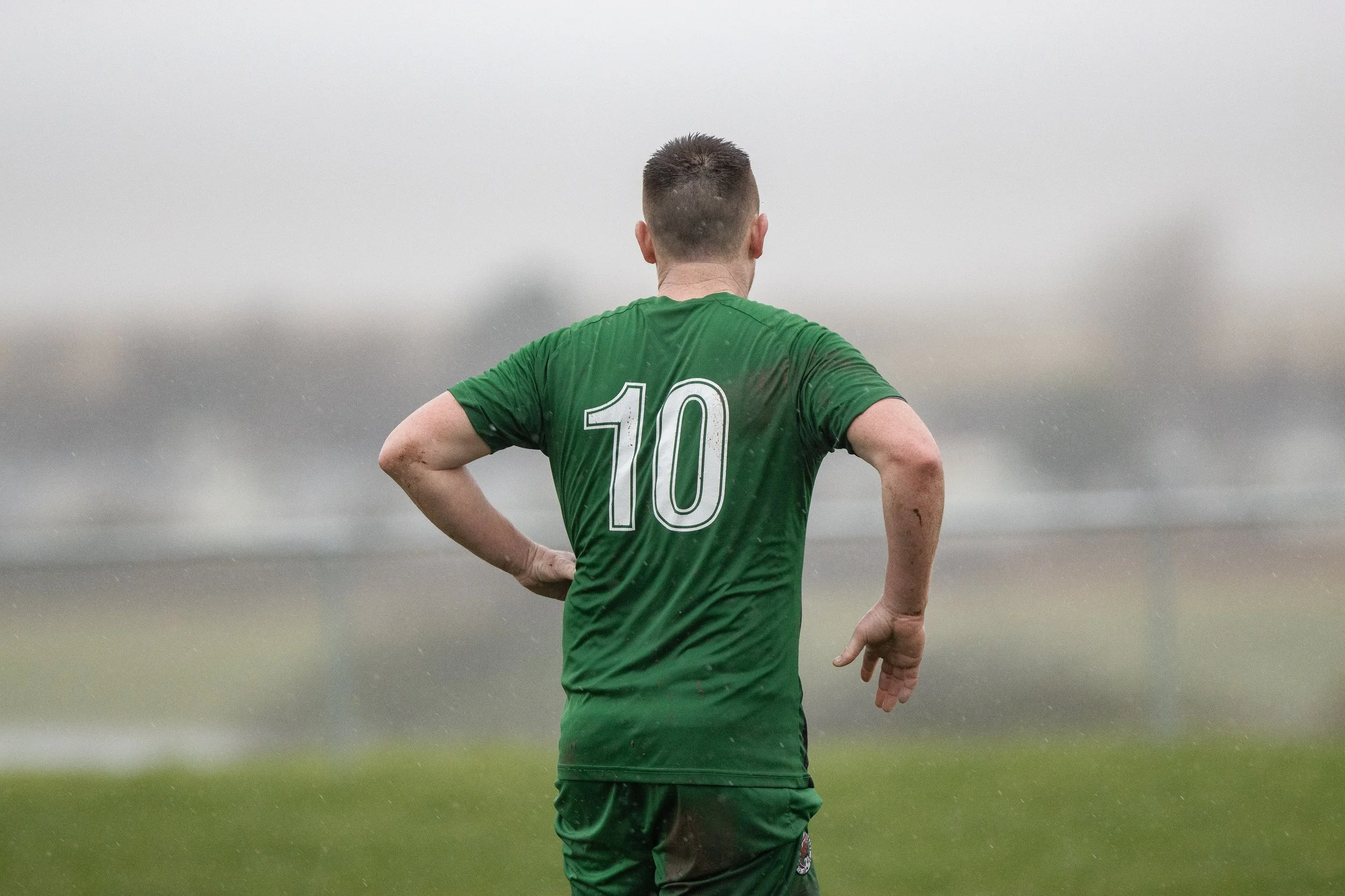 A soccer player wearing a green jersey with the number 10 on the back stands outdoors on a rainy day.