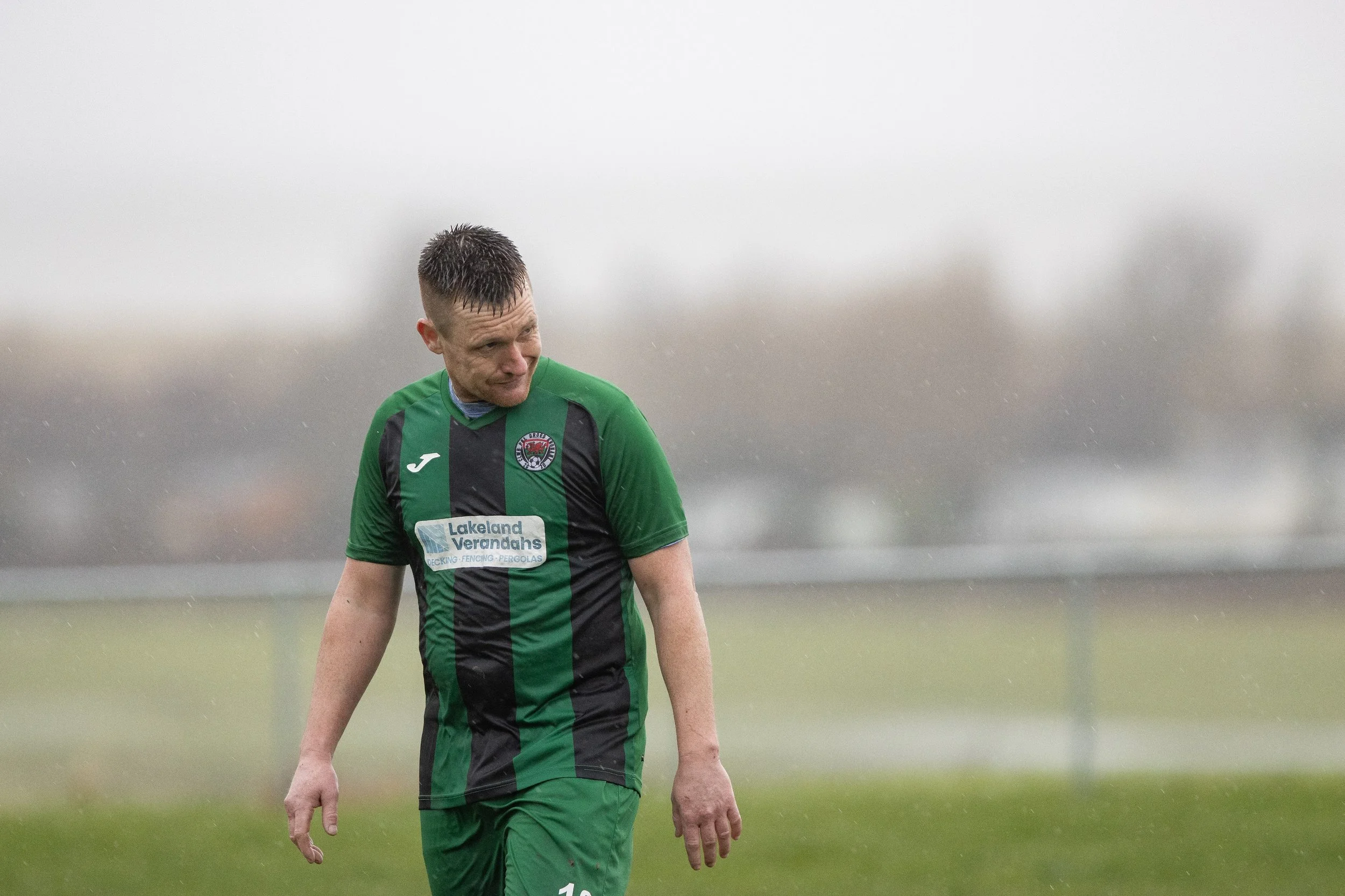 A male soccer player in a green and black uniform walking on a rainy field.