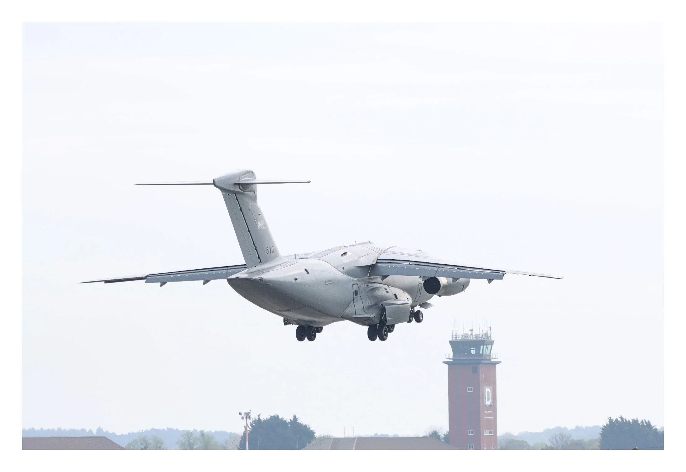 Military transport aircraft flying near an airport control tower.