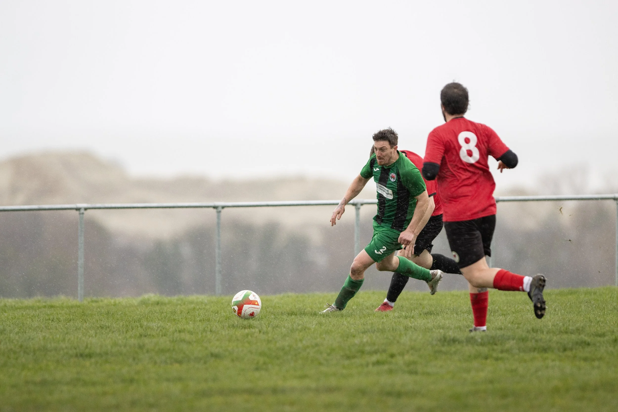 Soccer players competing for the ball on a grassy field during a game in rainy weather.