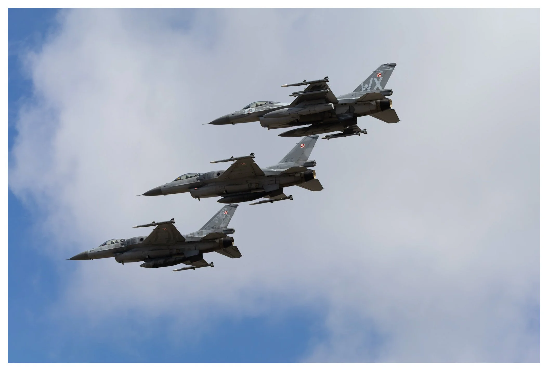 Three fighter jets flying in close formation through the sky with clouds in the background.