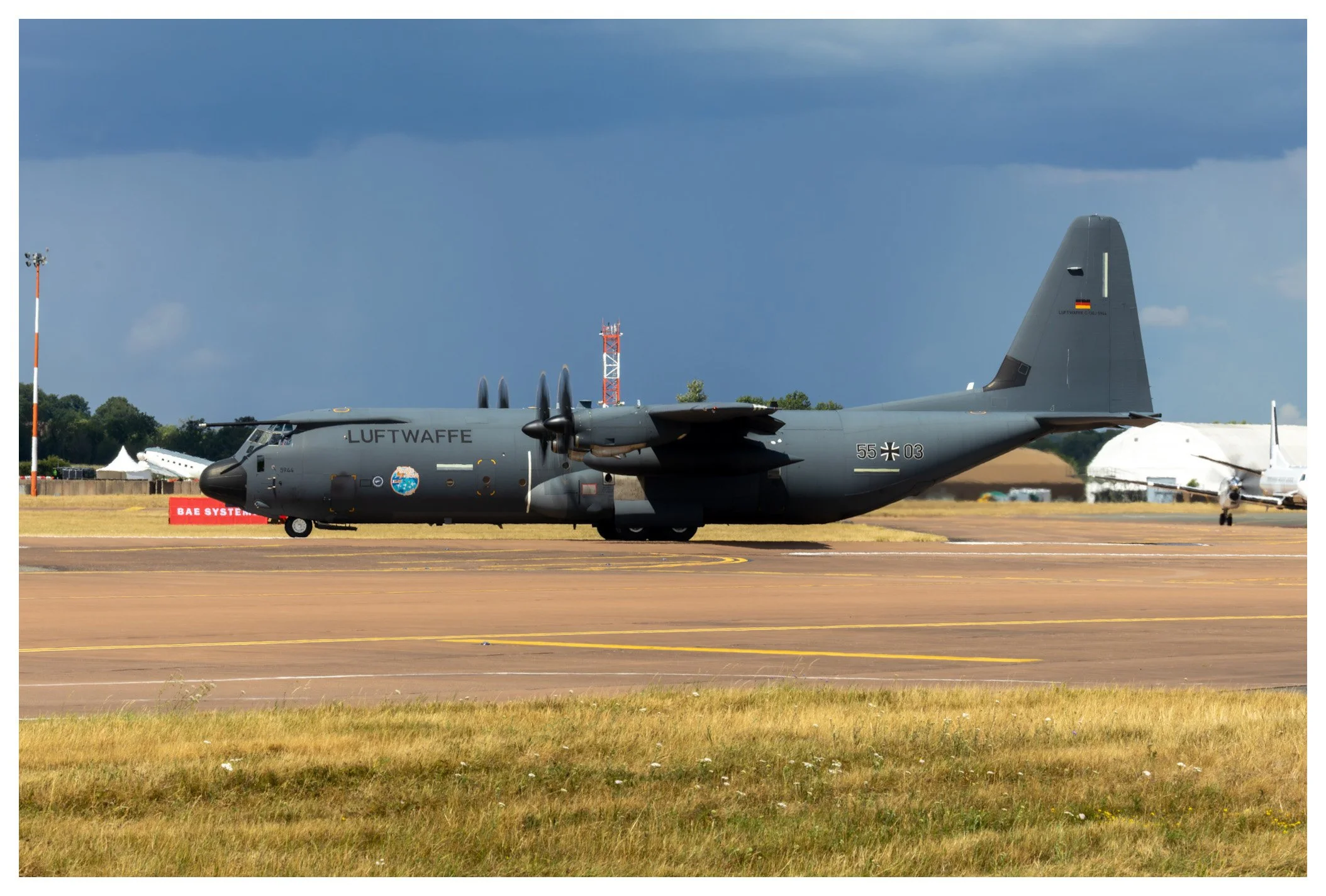 A military cargo aircraft on the runway with the text 'LUFTWAFFE' painted on the side and the German flag on the tail, during daytime with cloudy sky.