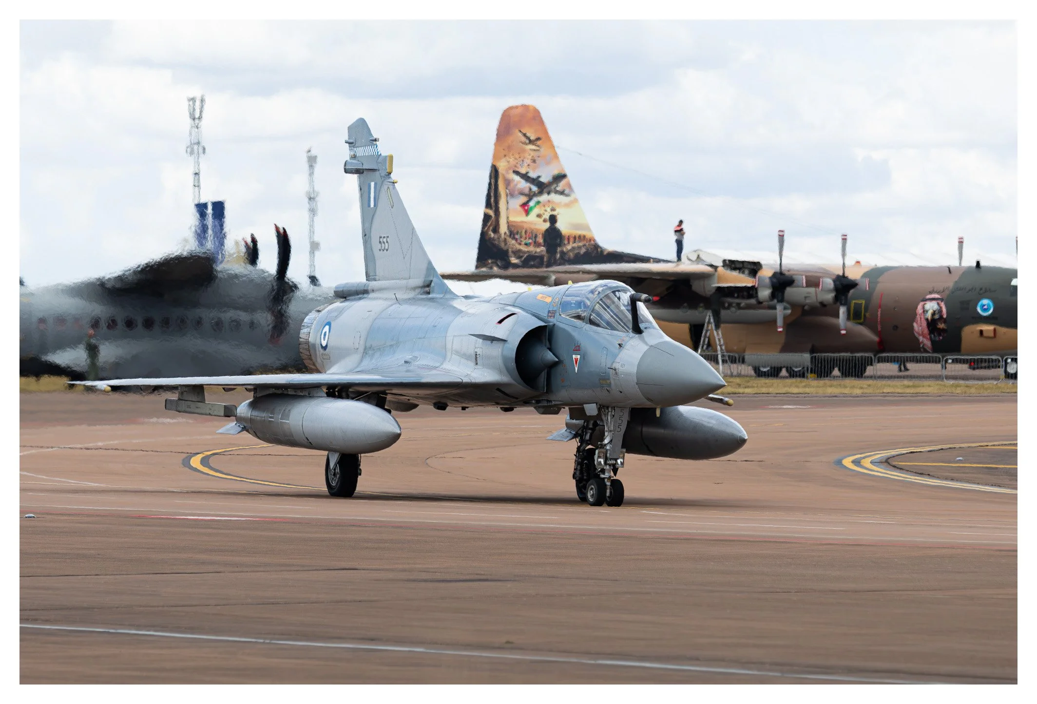 A military fighter jet on the tarmac with painted military aircraft and a mural in the background.
