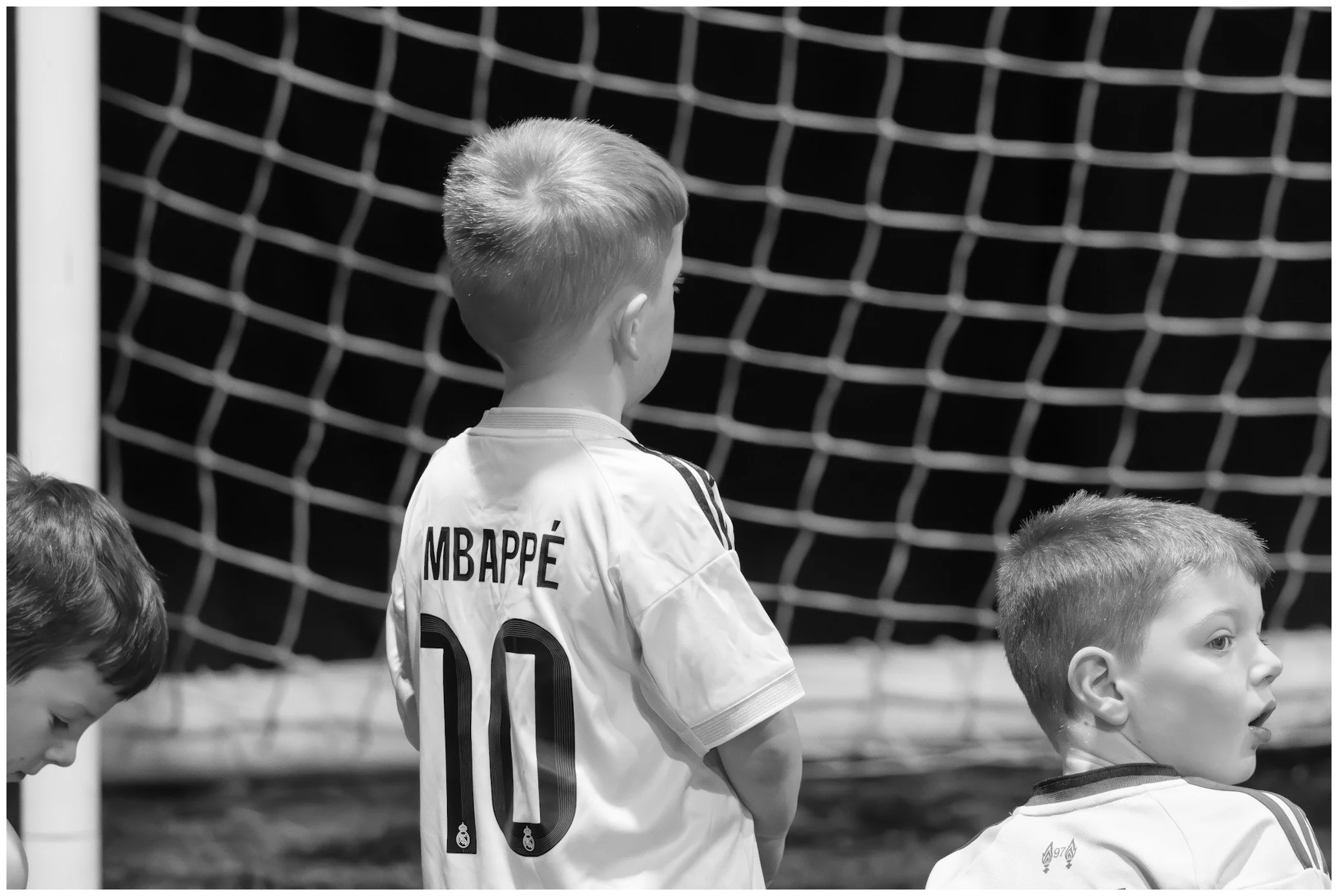 Young boys wearing soccer uniforms, one with the name 'MBAPPÉ' and number '10' on the back, standing near a soccer goal net.