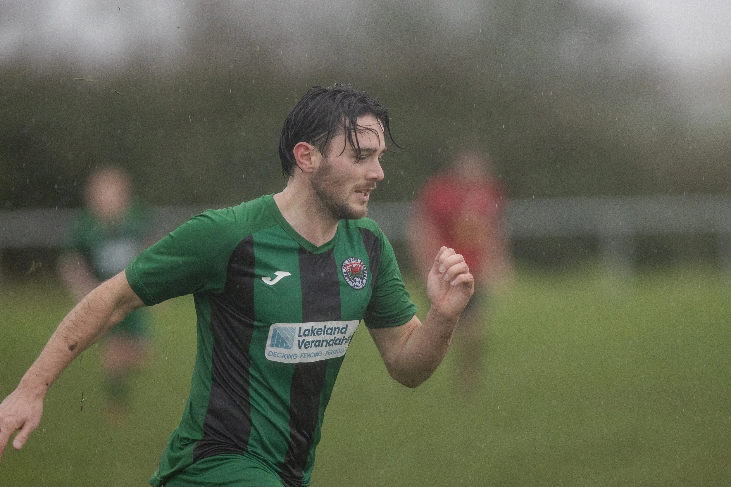 A male soccer player in a green and black uniform running in the rain during a match.