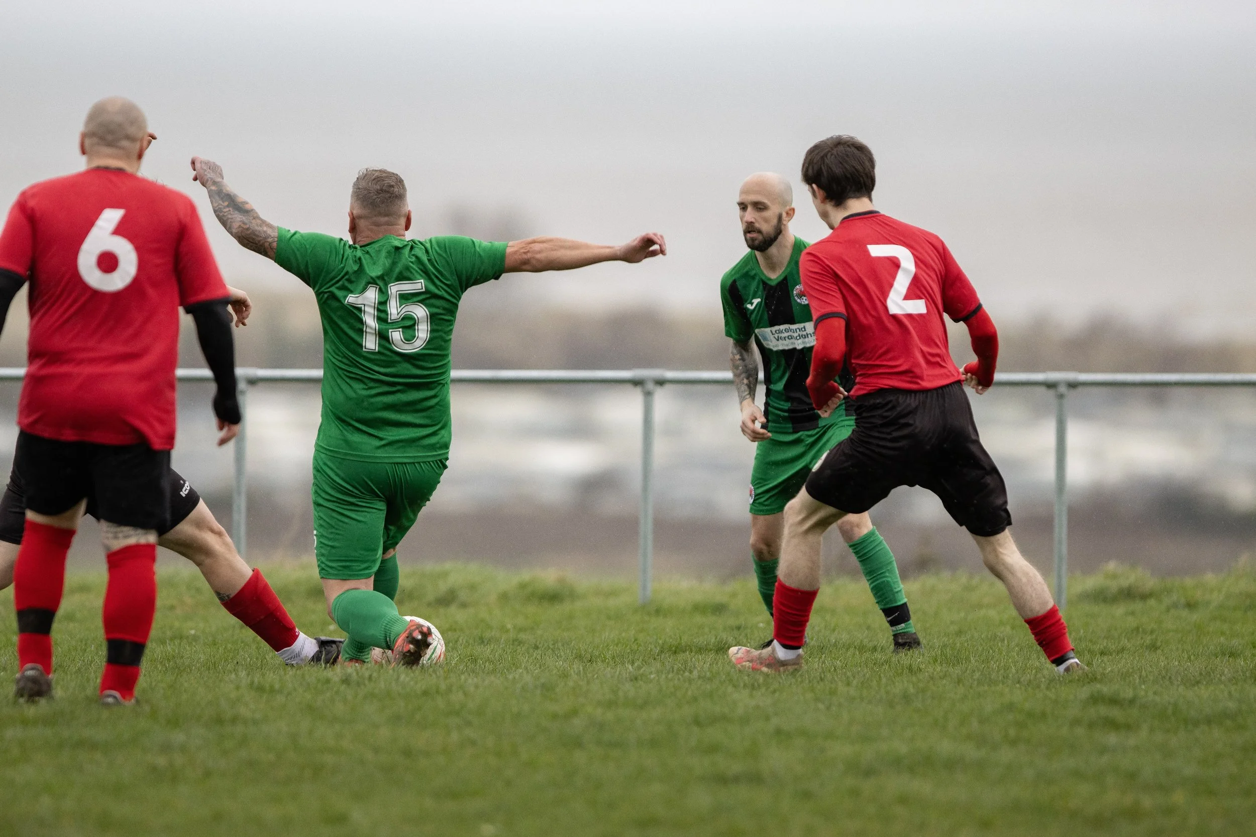 Soccer players in green and red jerseys competing for the ball on a grassy field.