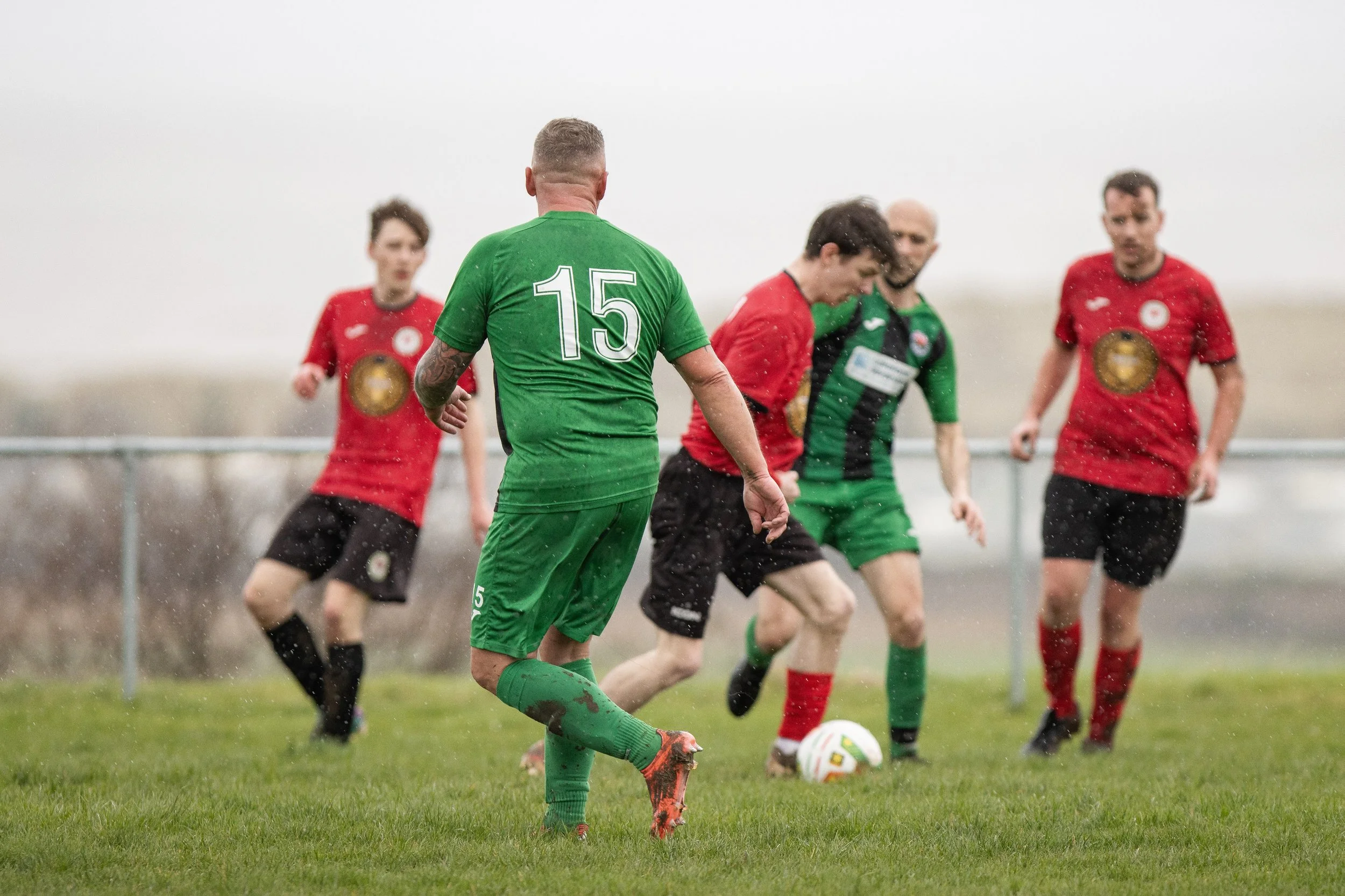 A soccer game on a rainy day with players actively competing for the ball on the field.
