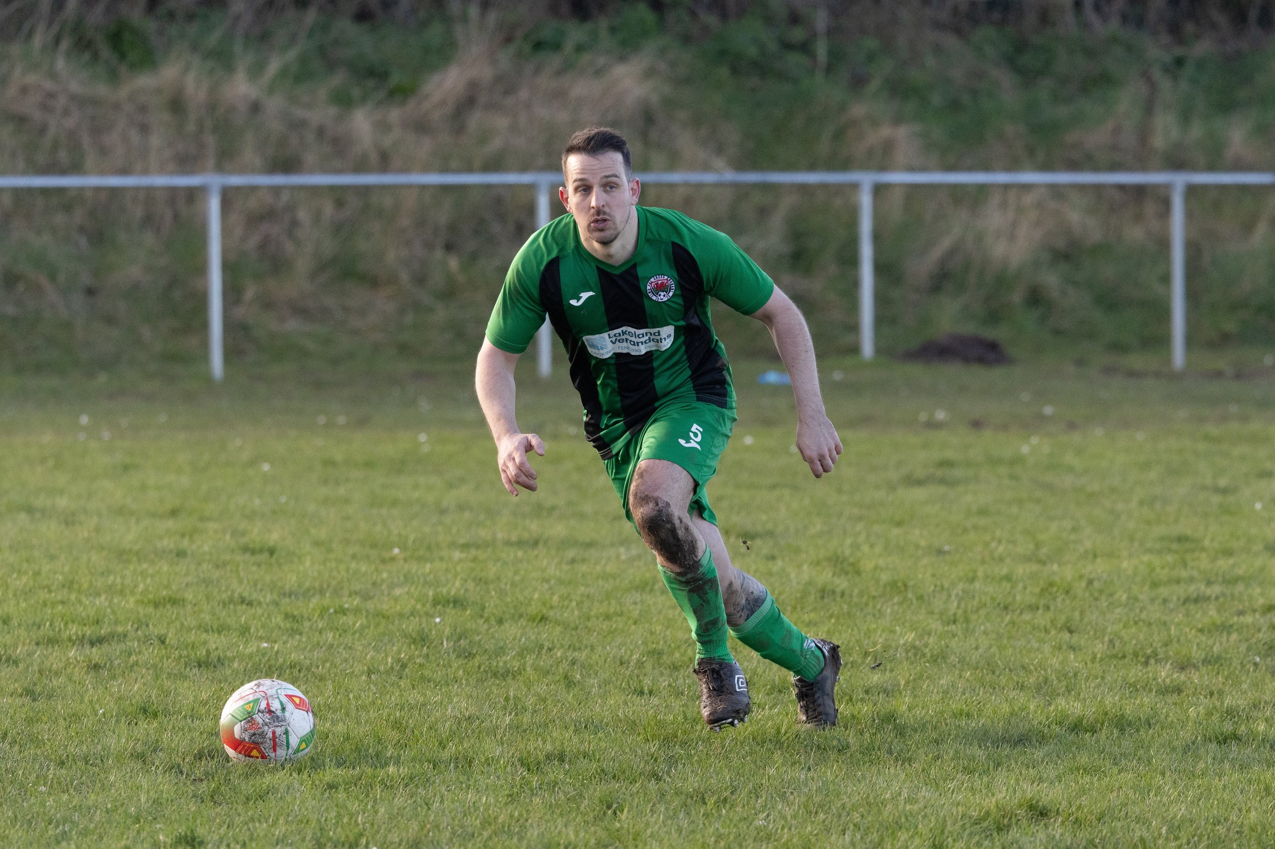 A man playing soccer on a grassy field, wearing a green and black uniform, with a soccer ball nearby.