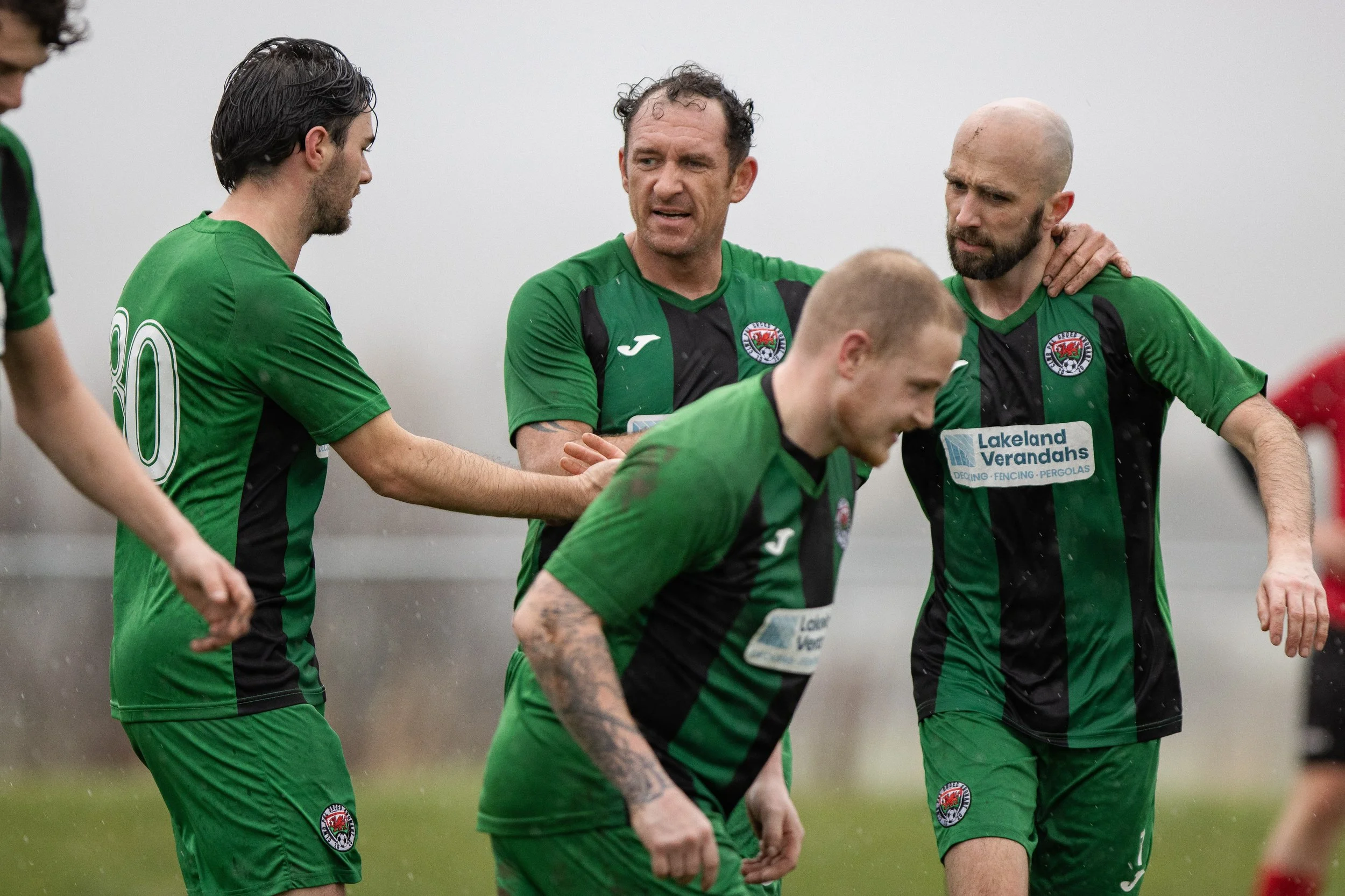 Soccer players in green and black uniforms on a field, some are smiling and comforting each other 