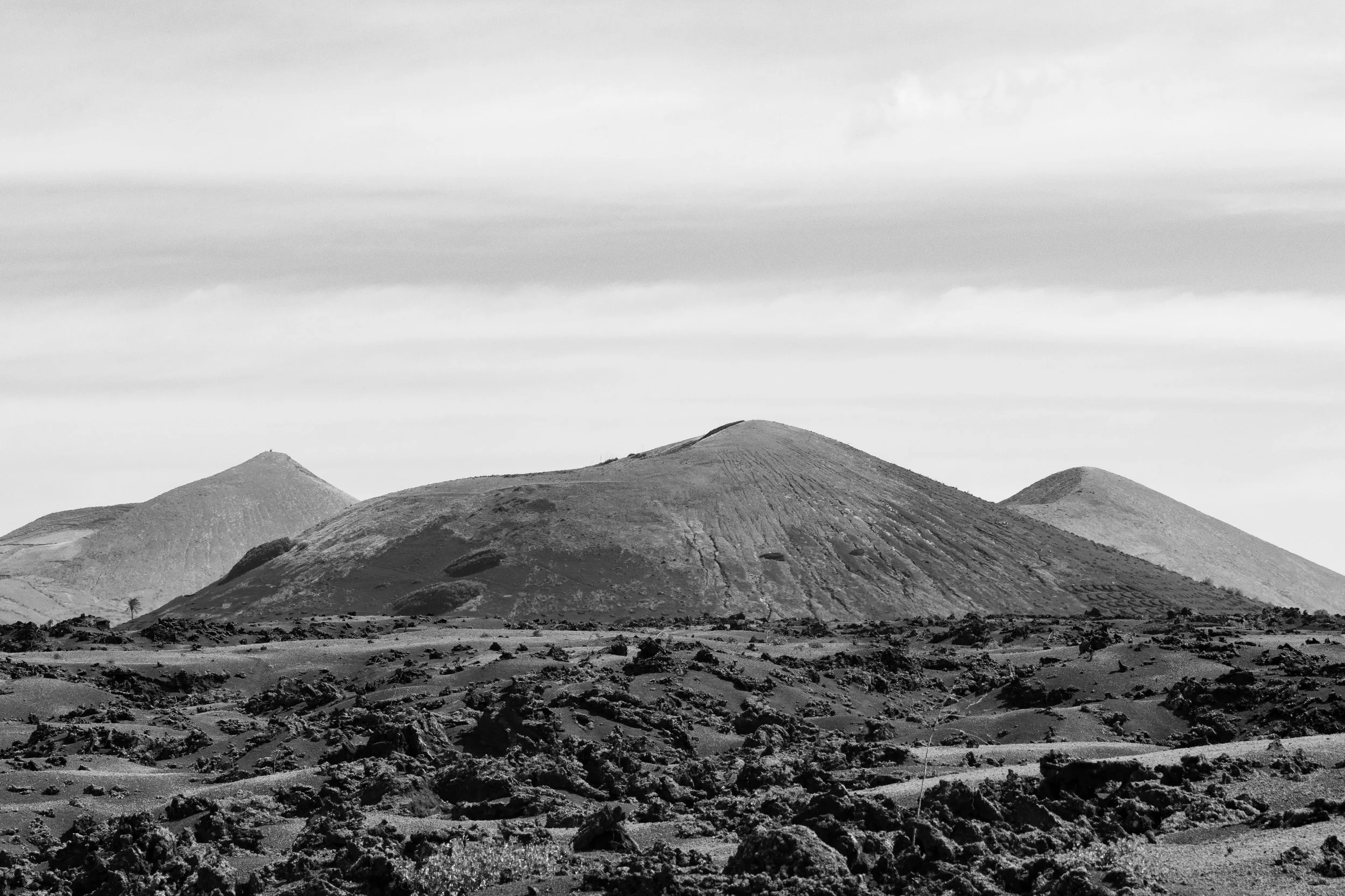 Black and white photo of a volcanic landscape with three prominent volcanoes and rugged, uneven terrain in the foreground.