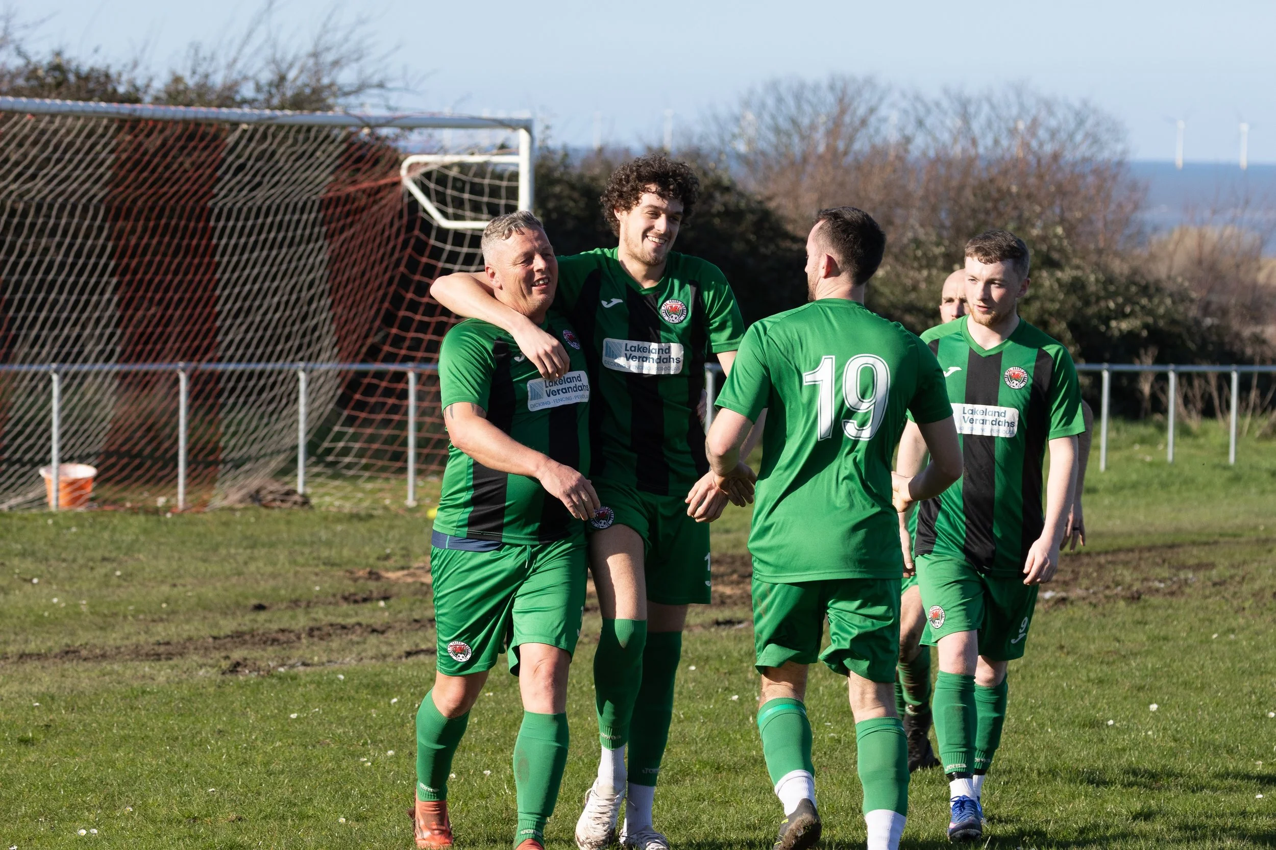 Soccer players in green uniforms celebrating on the field after scoring