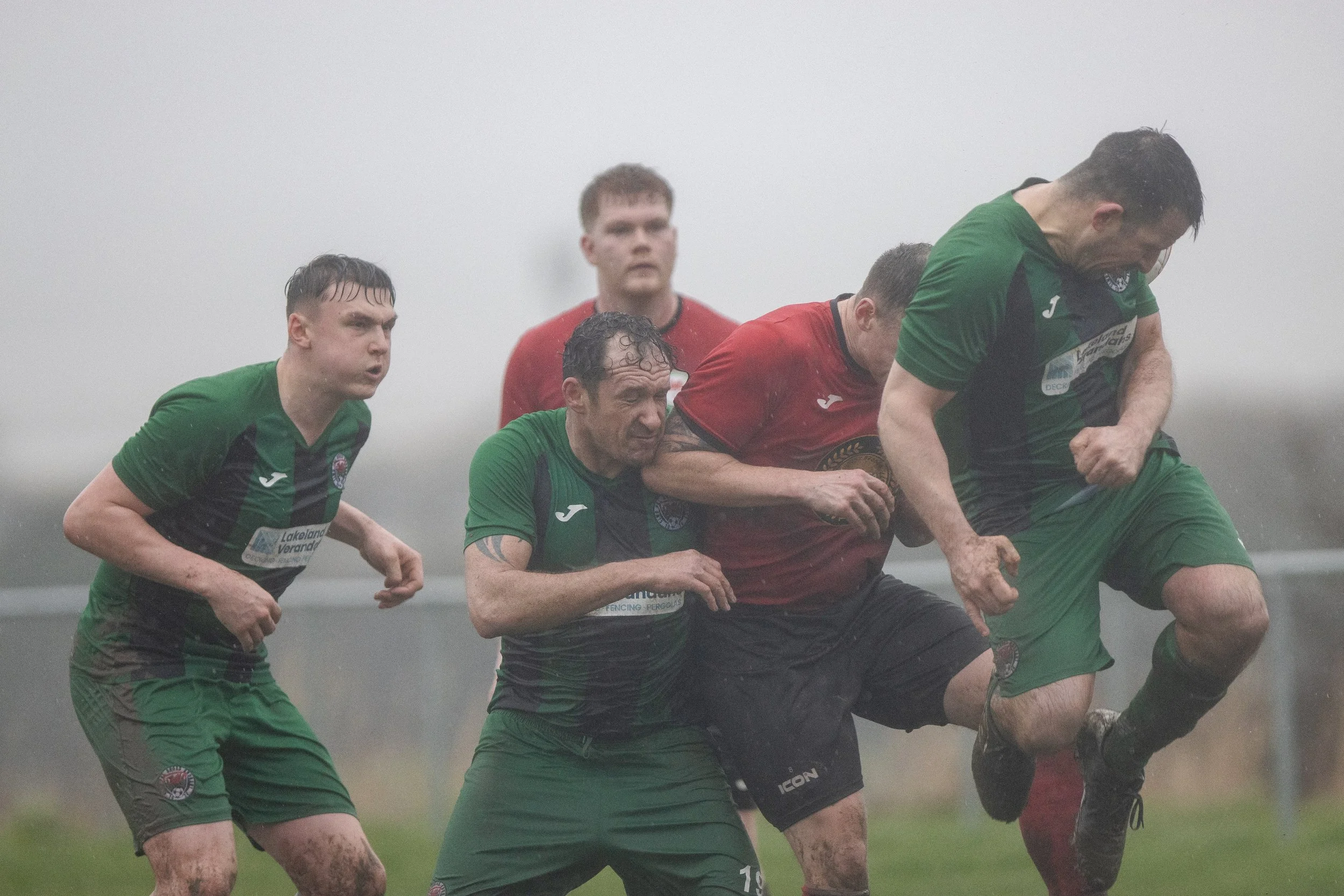 Rugby players in green and red uniforms competing during a match in rainy weather.