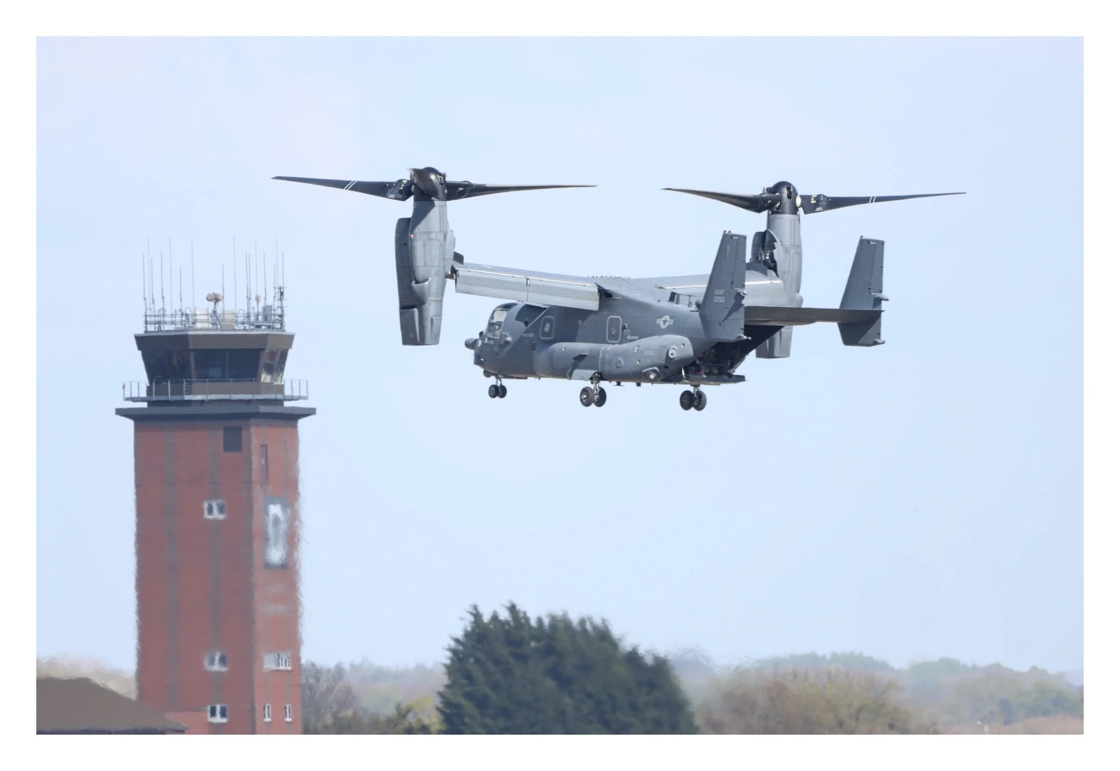 An Osprey V-22 tiltrotor aircraft flying near a tall control tower at an airport.