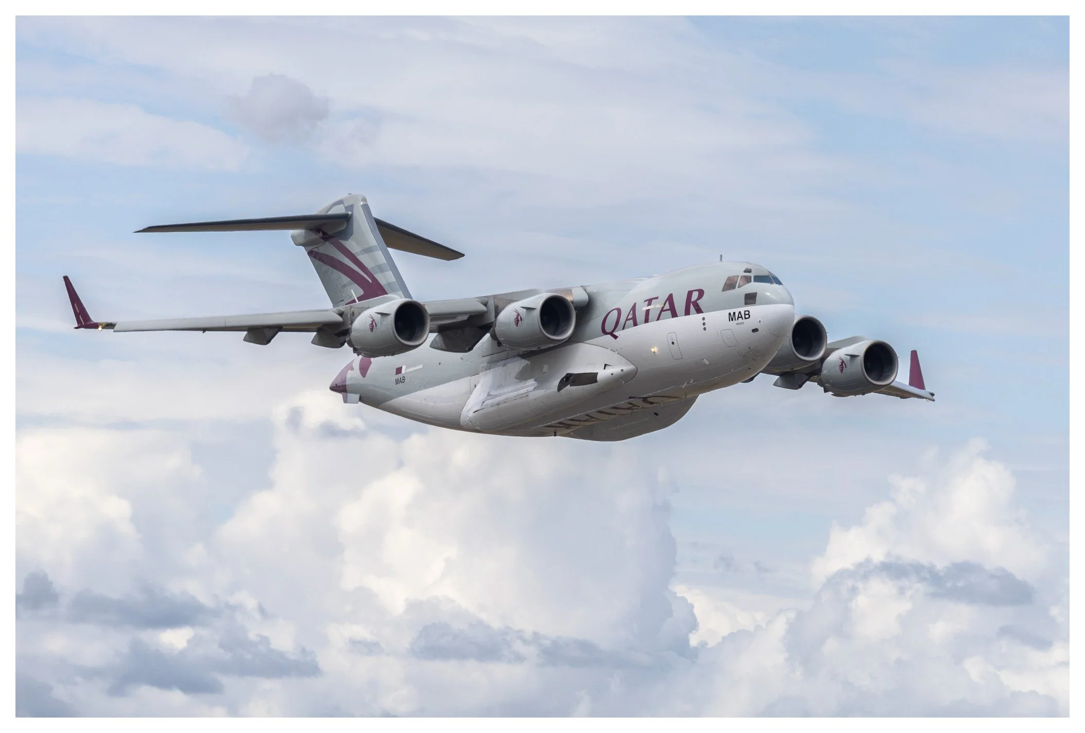 A Qatar Airways cargo plane flying in the sky with clouds in the background.
