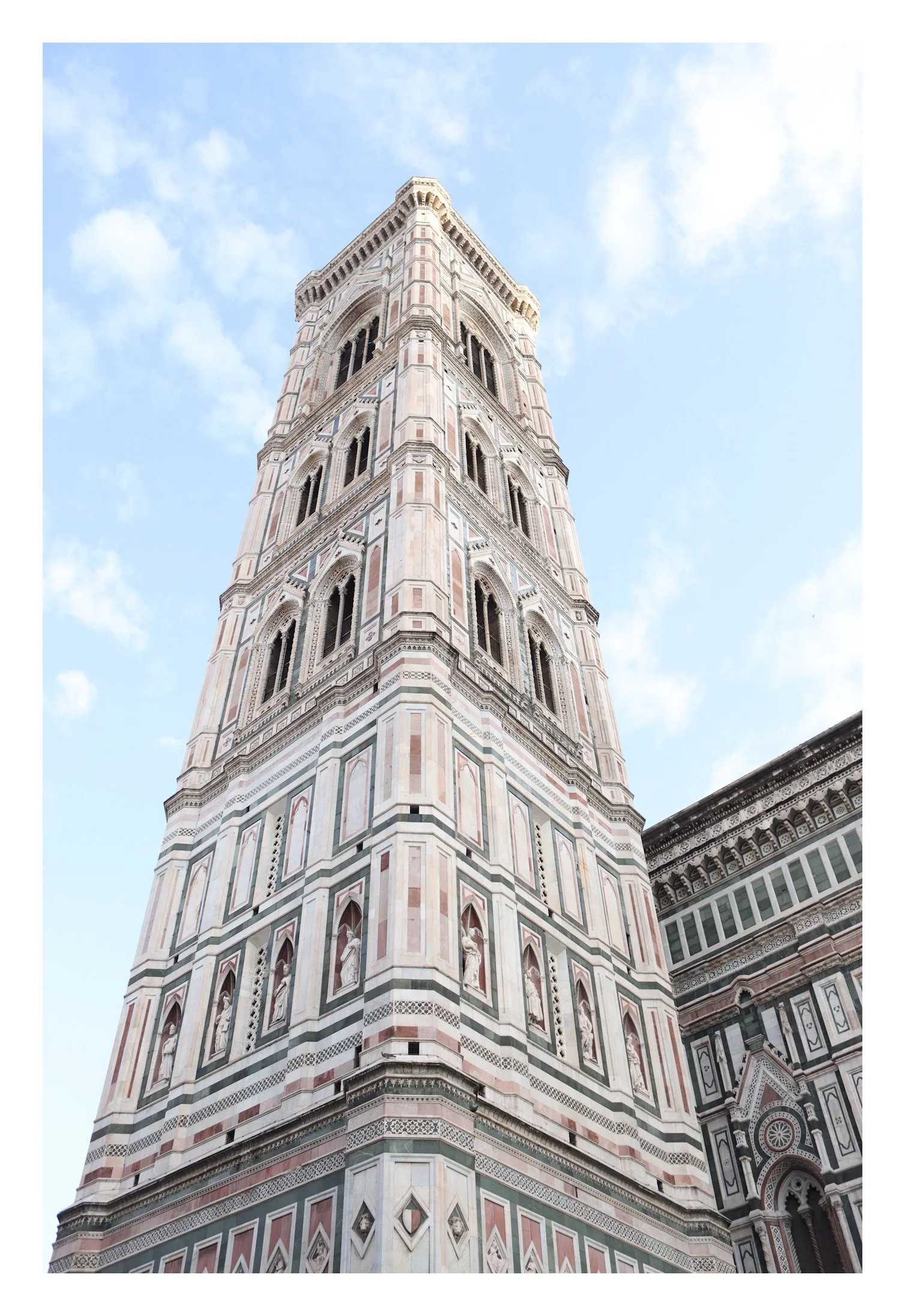 Photograph of the Campanile di Giotto, a tall, ornate bell tower at Florence Cathedral in Florence, Italy, with a bright blue sky in the background.